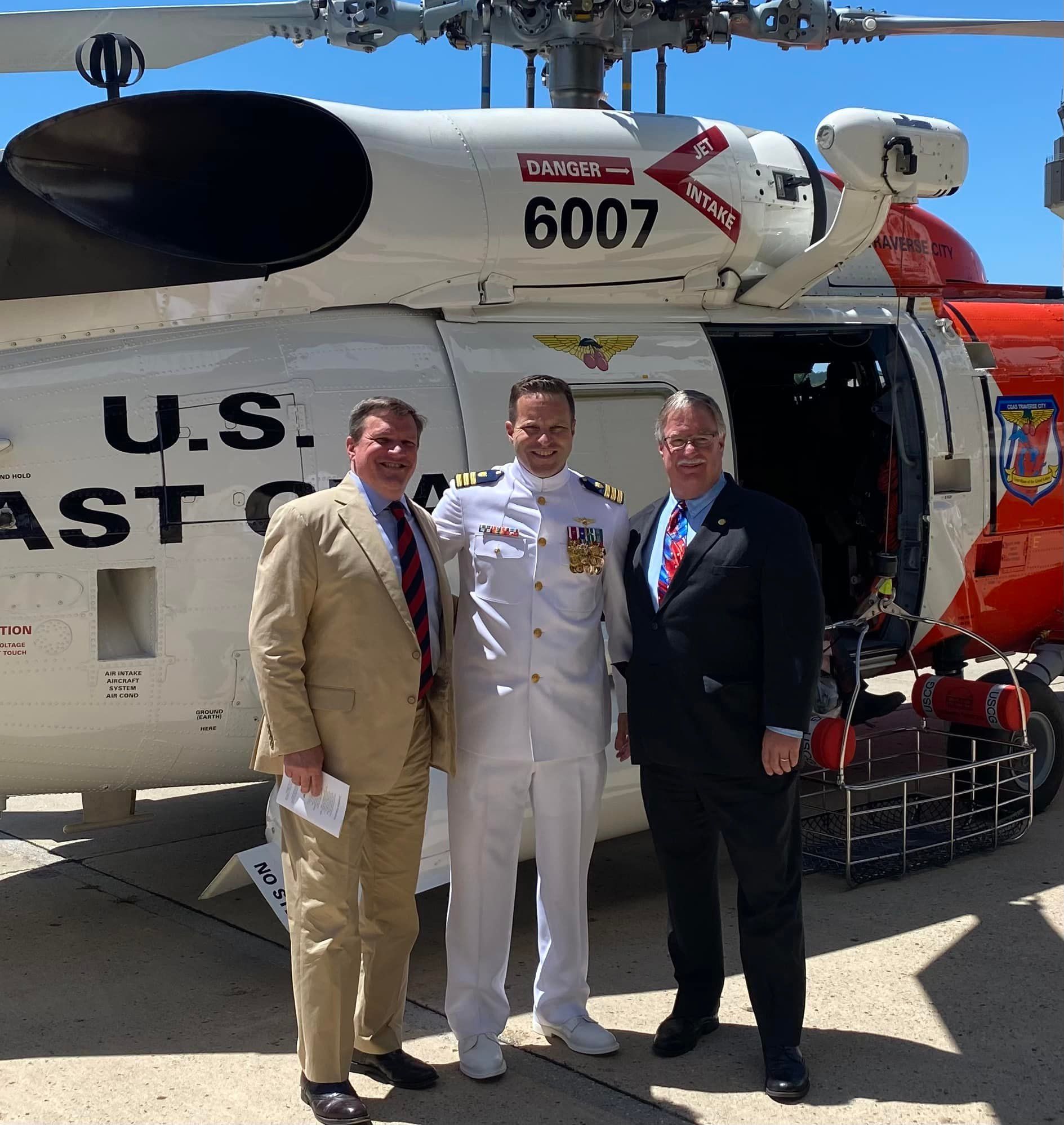 Three men standing in front of a u.s. coast guard helicopter - John Roth