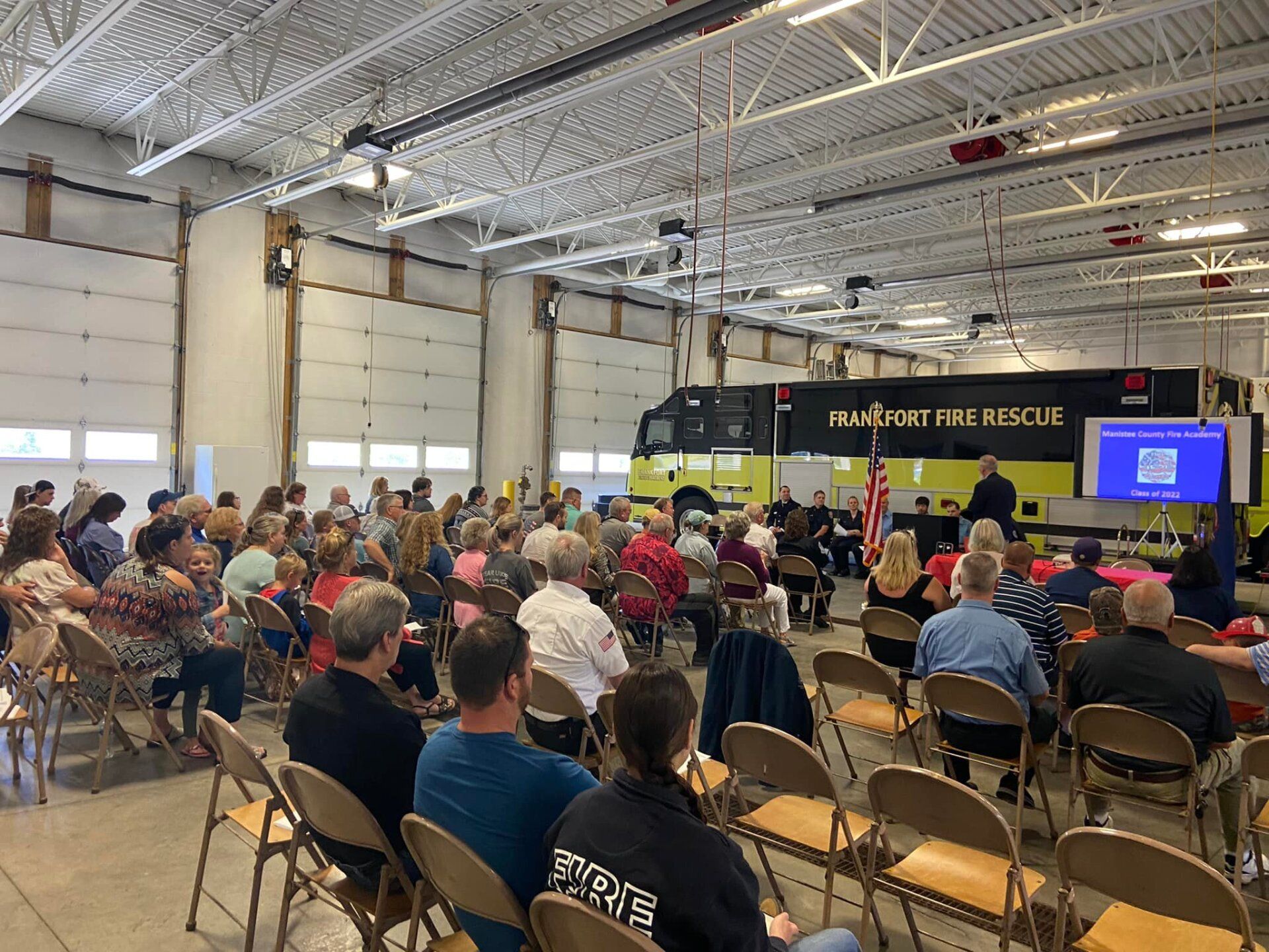 A large group of people are sitting in chairs in front of a fire truck.