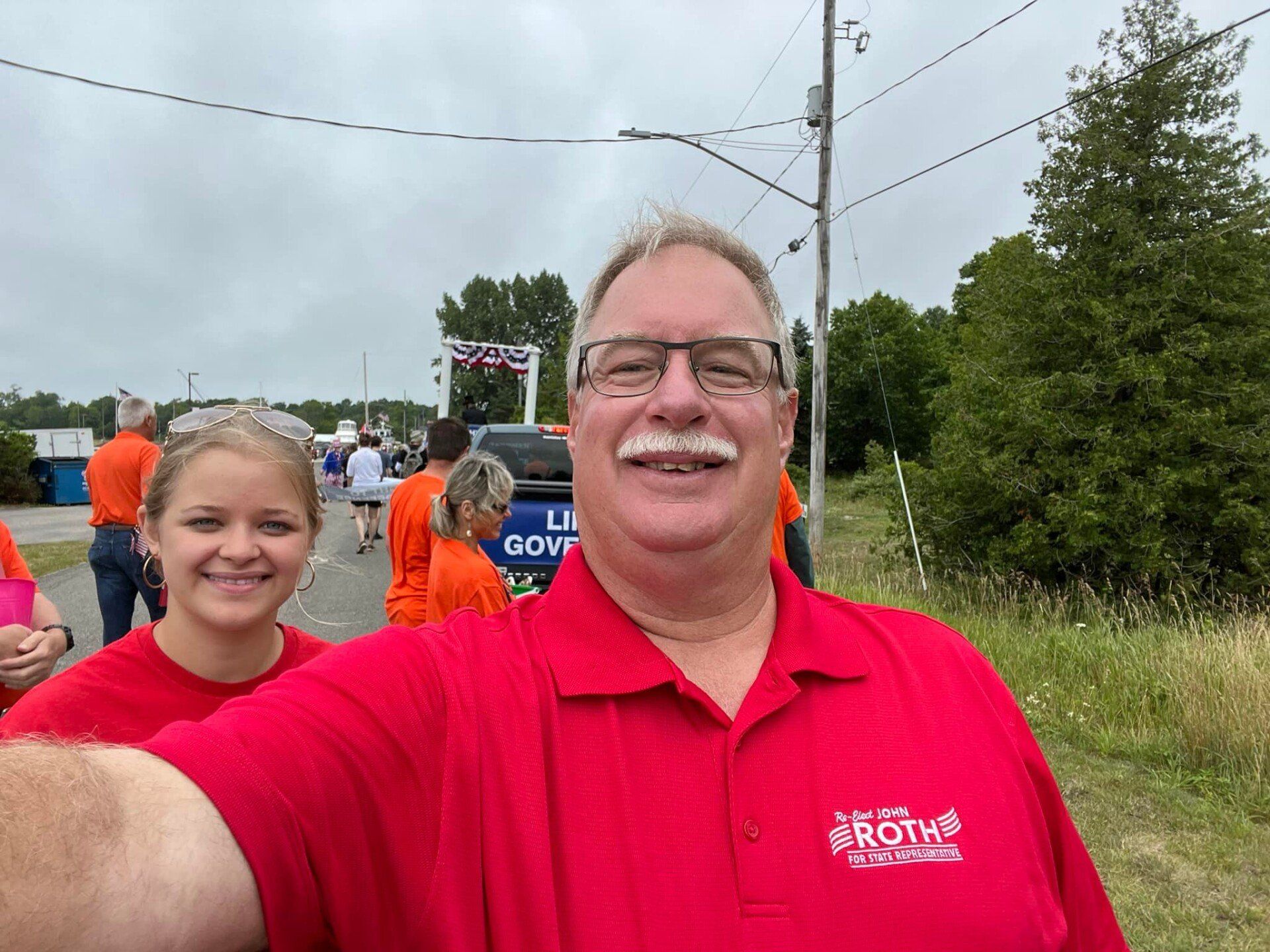 John Roth is taking a selfie with a woman in an orange shirt.