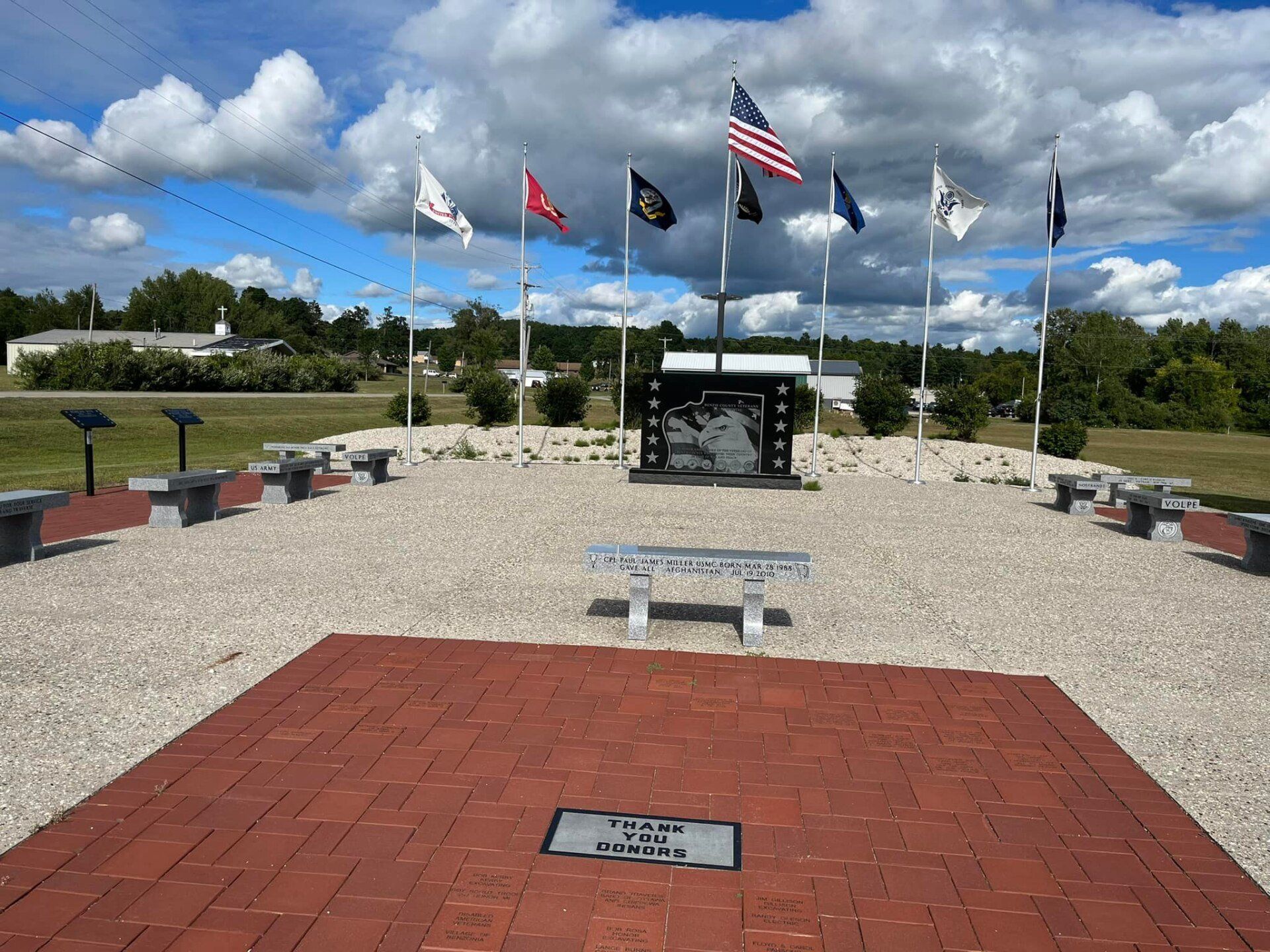 A brick walkway with a memorial in the middle and flags flying in the background.
