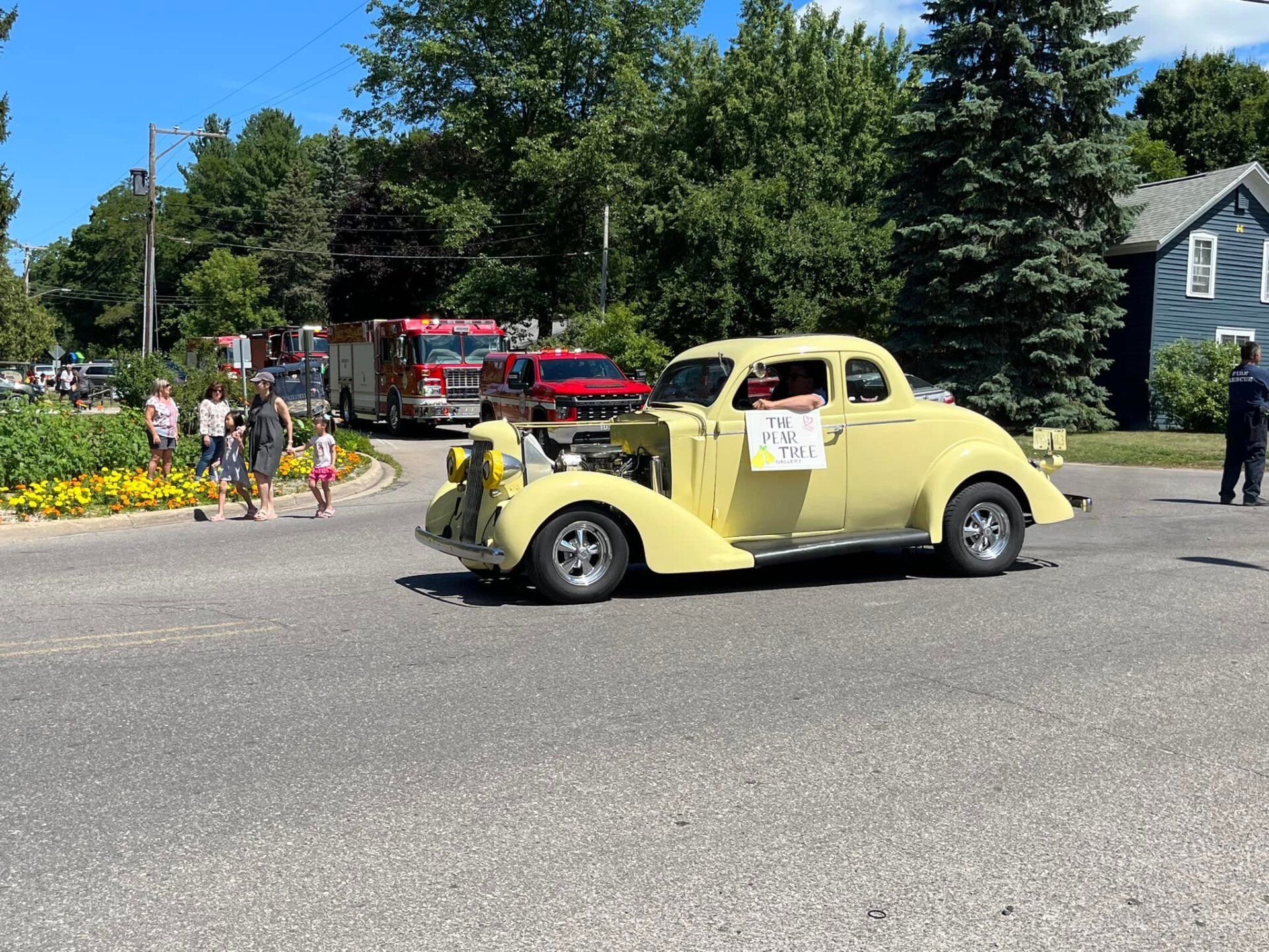 A yellow car is driving down a street in a parade.