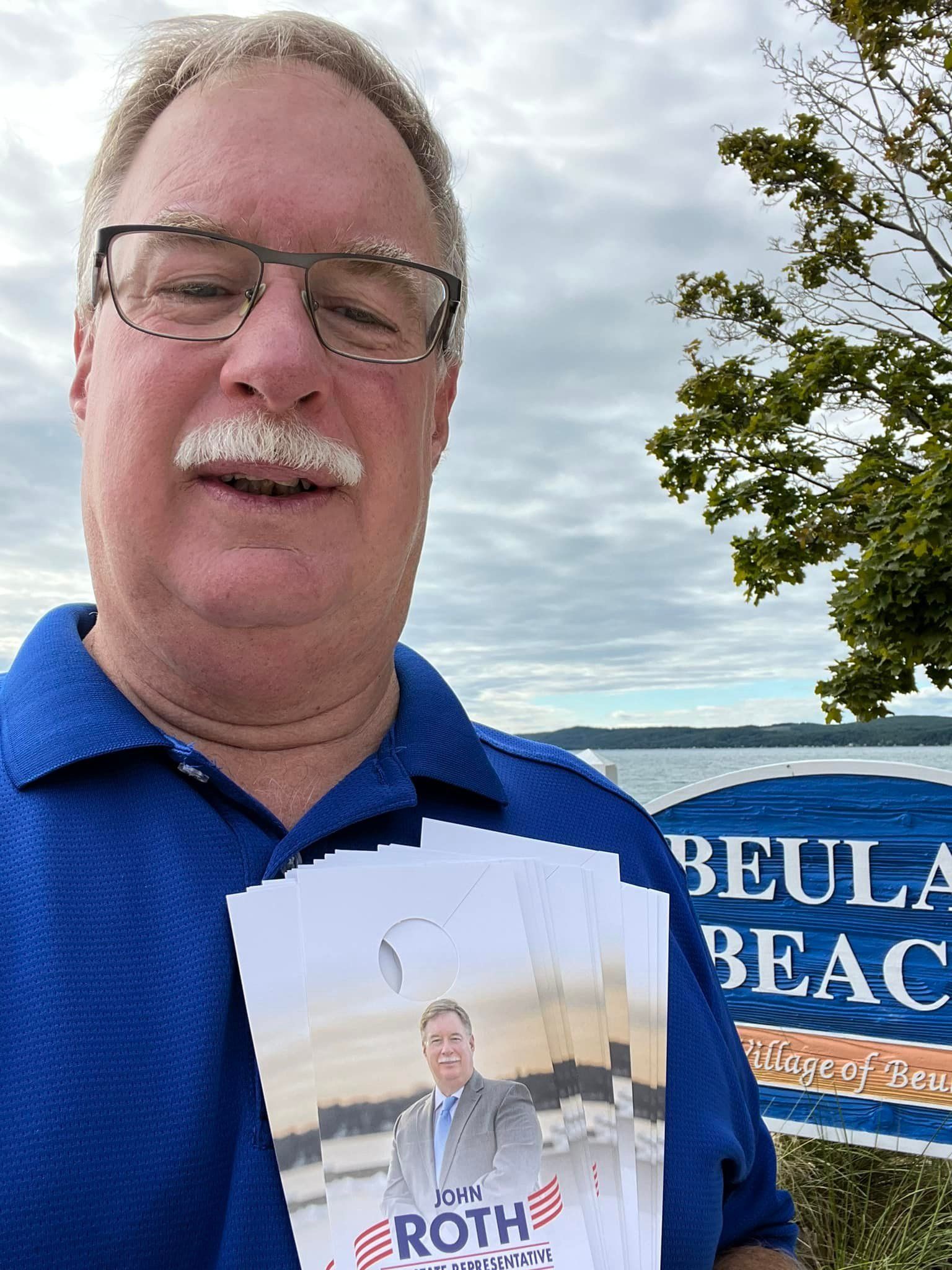 John Roth is holding a book in front of a sign.