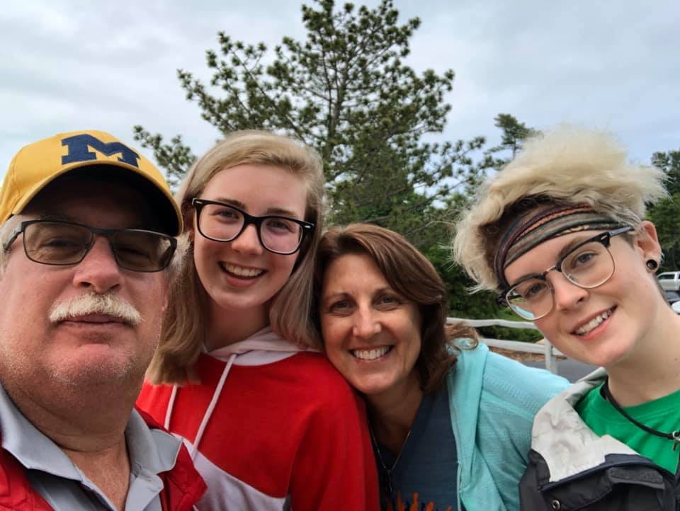 John Roth wearing a yellow hat with the letter m on it is posing for a picture with his family.