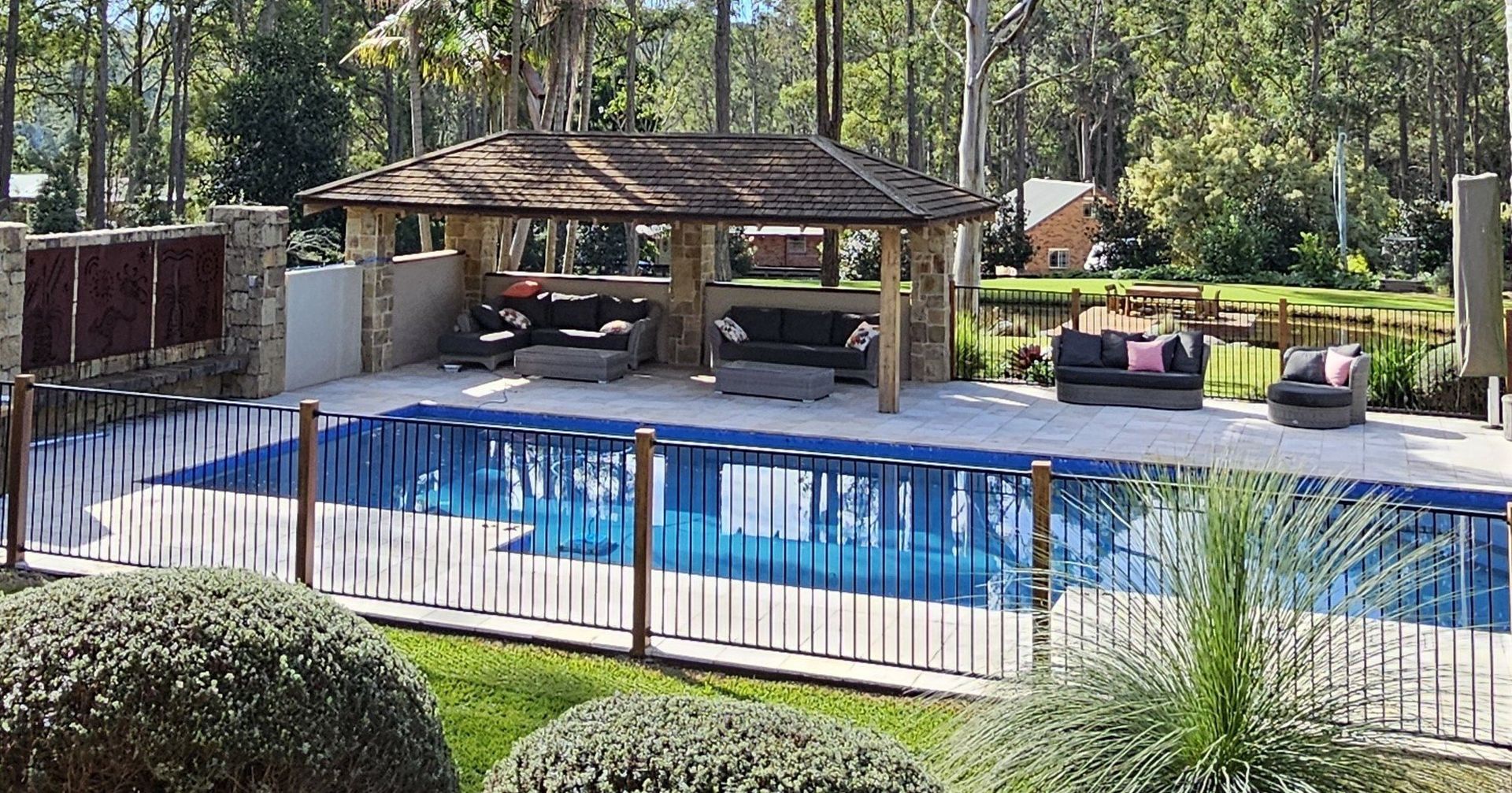 Gazebo under construction near a swimming pool. Wooden roof and support beams, stone pillars.
