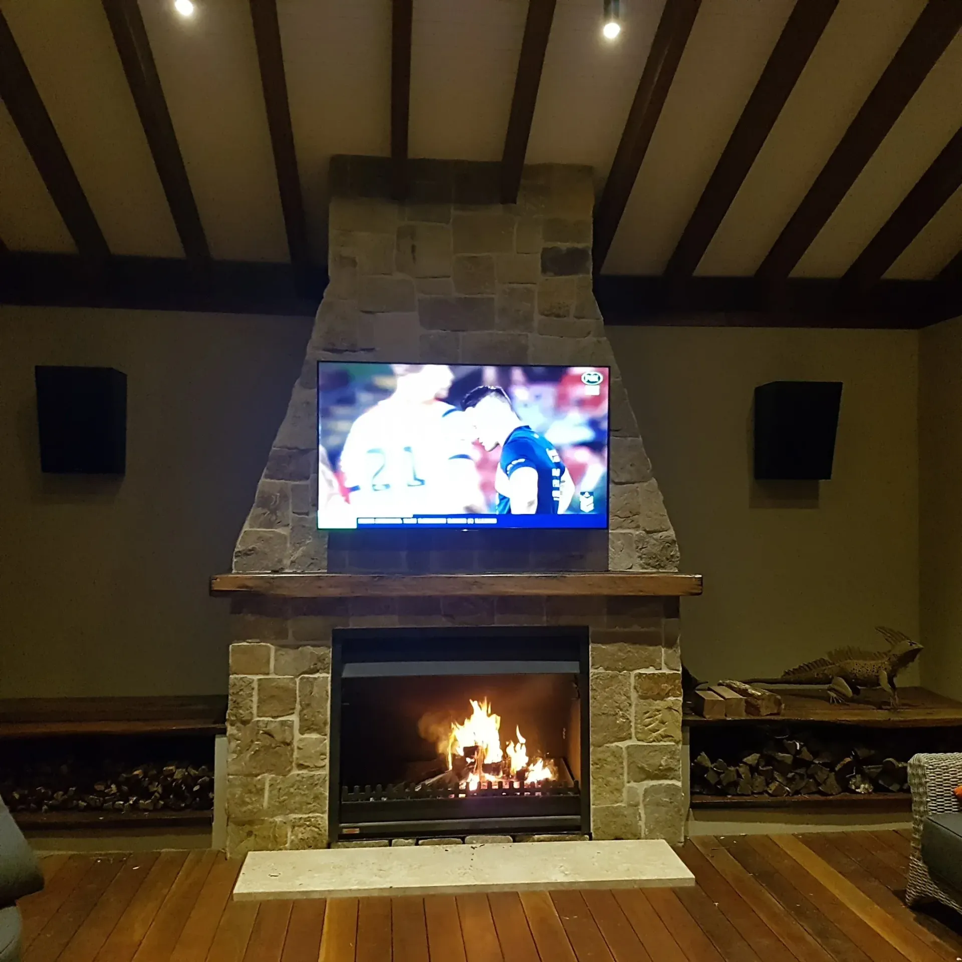 Fireplace with a TV above it, flames burning in the hearth. Speakers flank the TV.