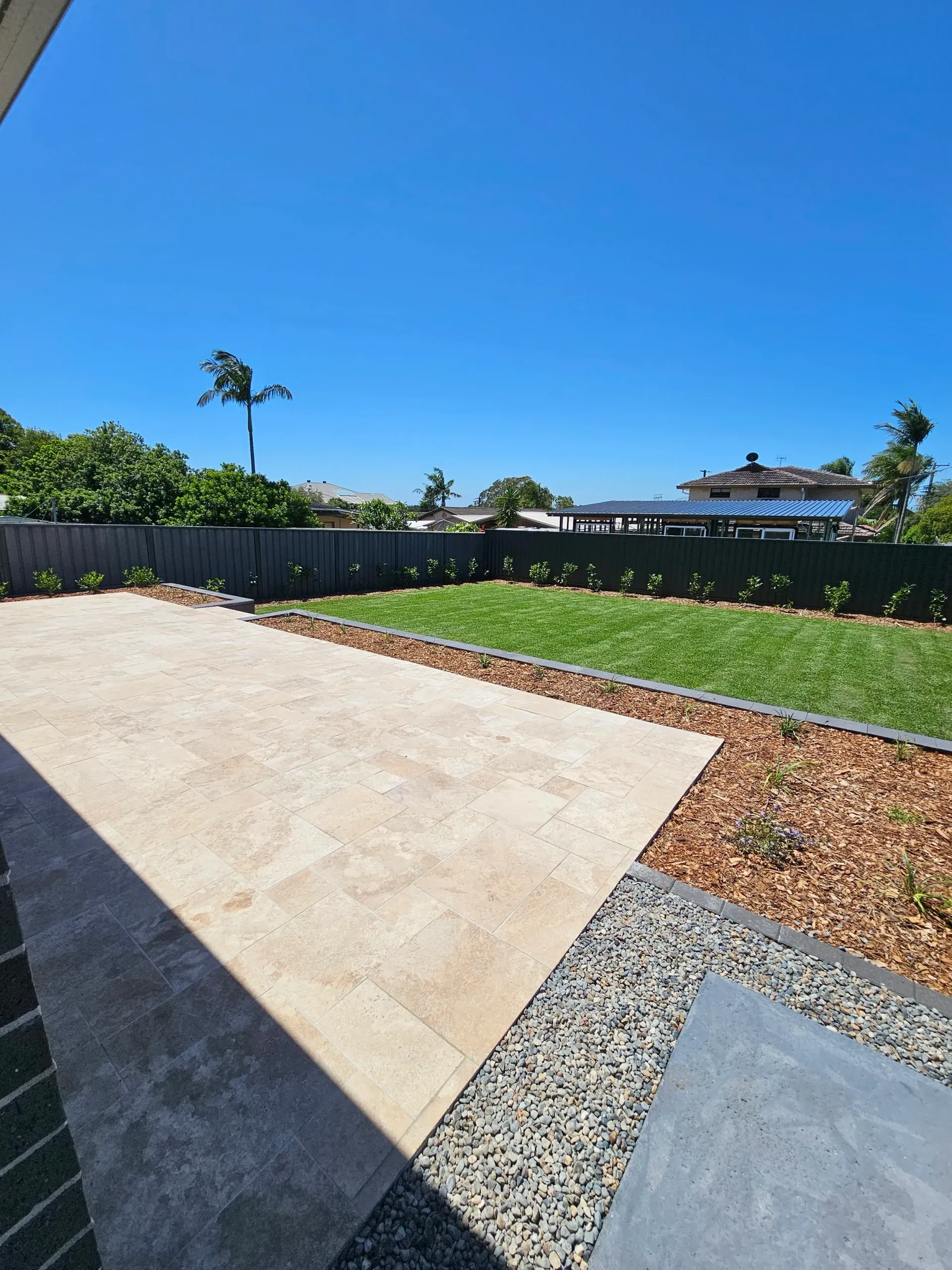 Patio with stone pavers, gravel border, and lawn under a blue sky.