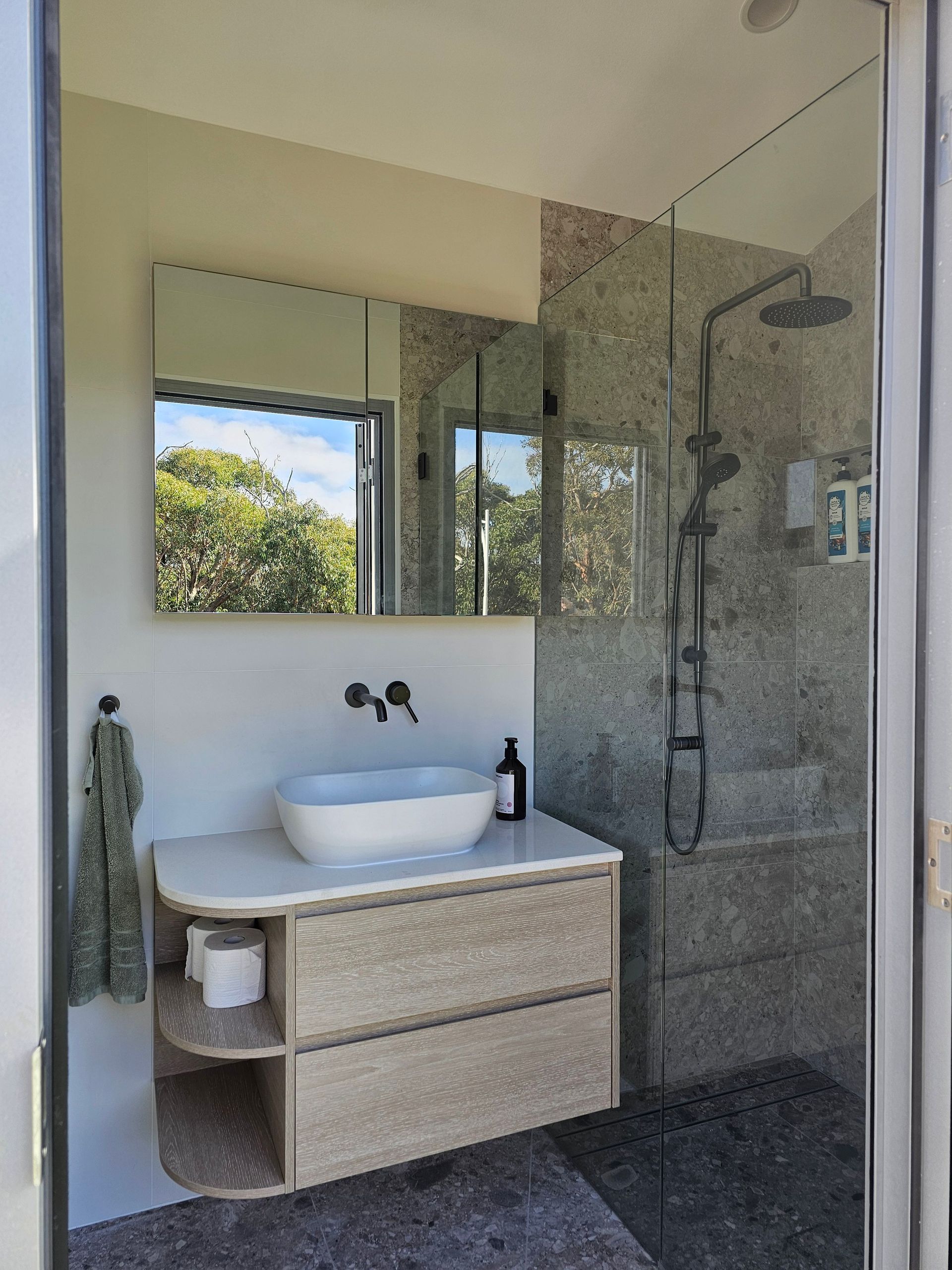 Bathroom with a vessel sink, wood vanity, and a pebble-tiled shower with glass doors.
