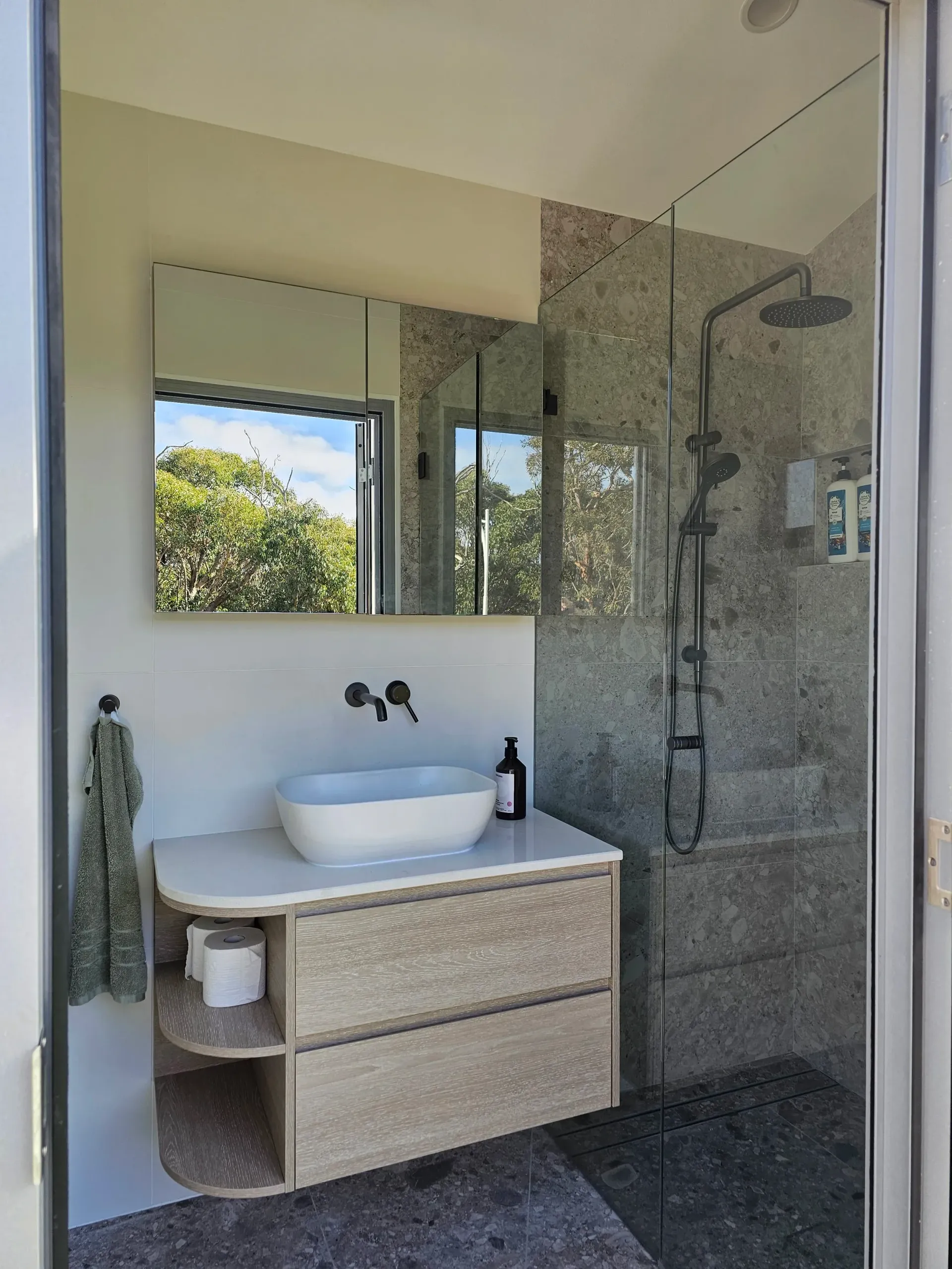 Bathroom with a vanity and a glass-enclosed shower. Vanity has a sink, drawers, and open shelving.