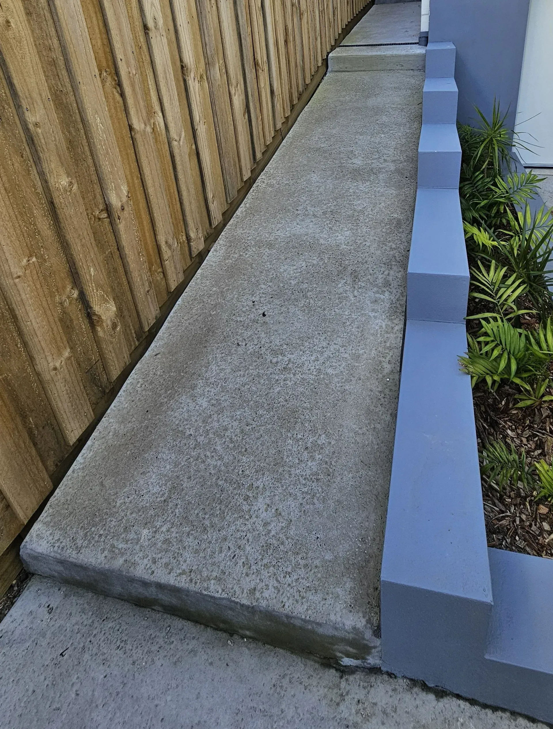 Concrete ramp alongside a wooden fence and tiered planters with greenery.