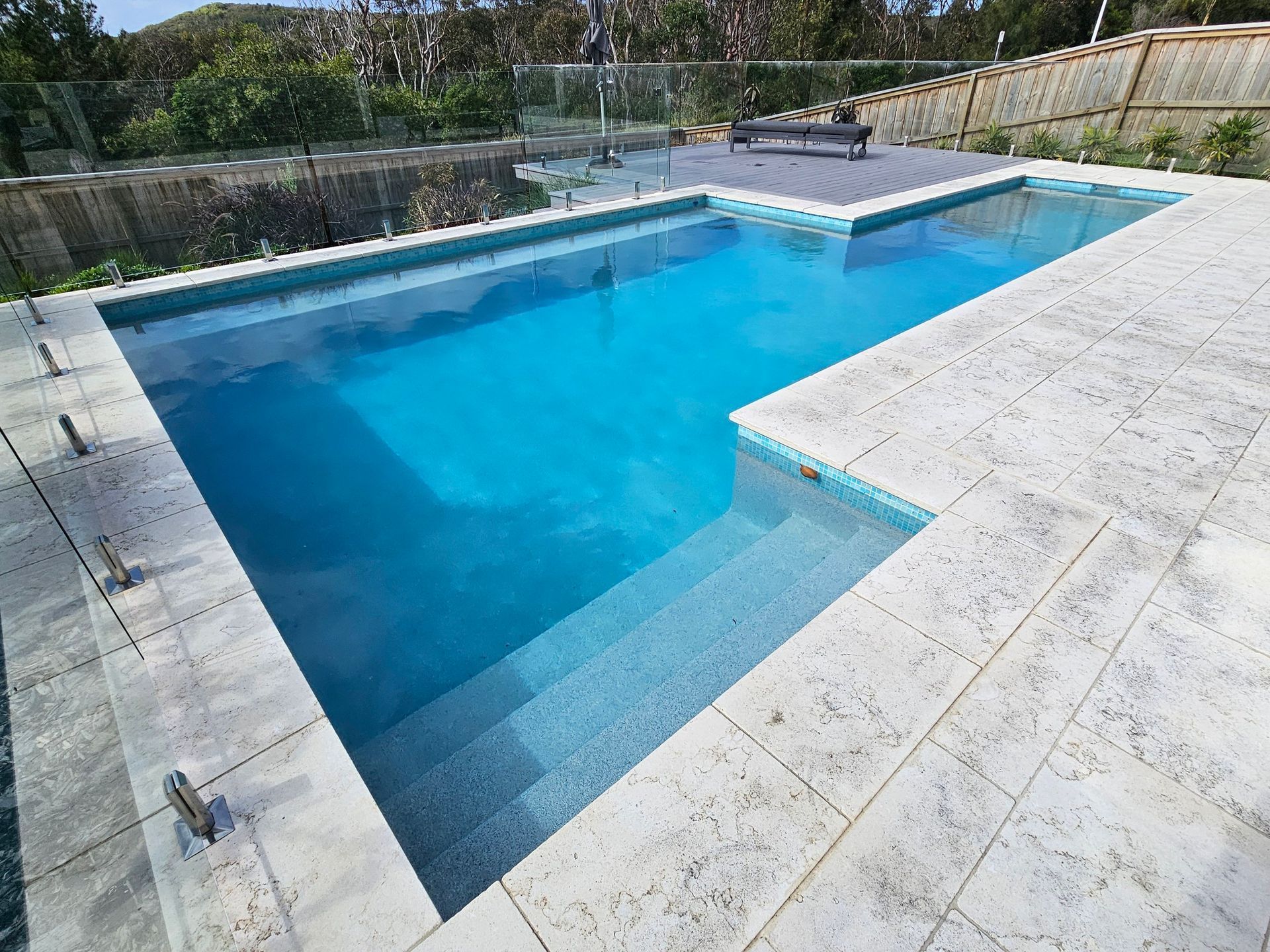 Rectangular swimming pool with light blue water and stone patio. Steps lead into the pool.