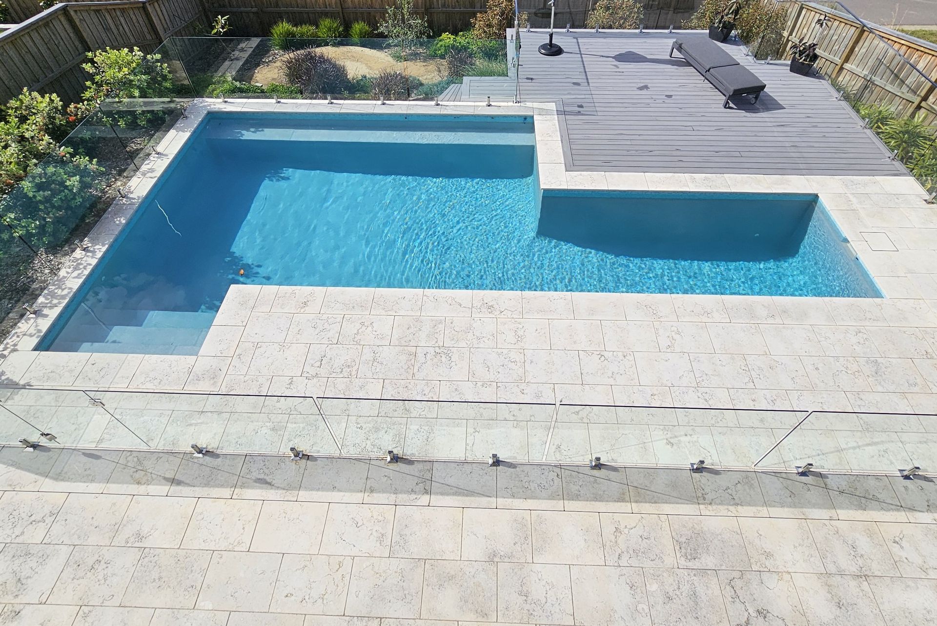 Swimming pool with blue water and light stone surround; wooden deck on the right.