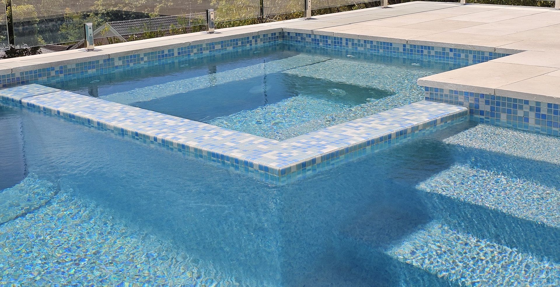 Blue-tiled swimming pool with a raised spa area; steps and surrounding concrete.