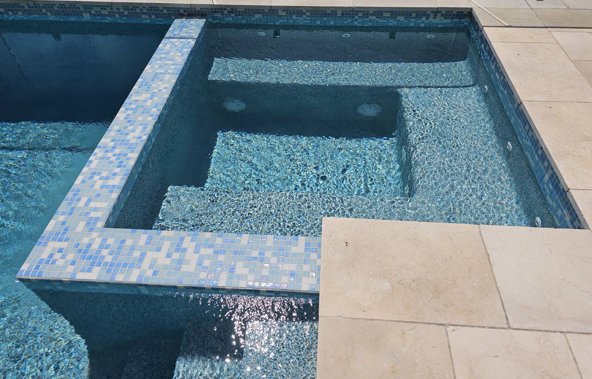 Pool with blue tile and steps, surrounded by light-colored stone.