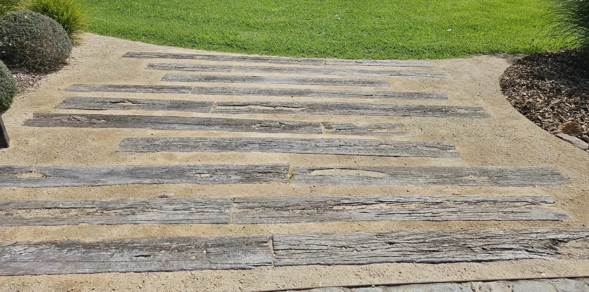 Stone path with grassy lawn on the right, and two round bushes on the left.