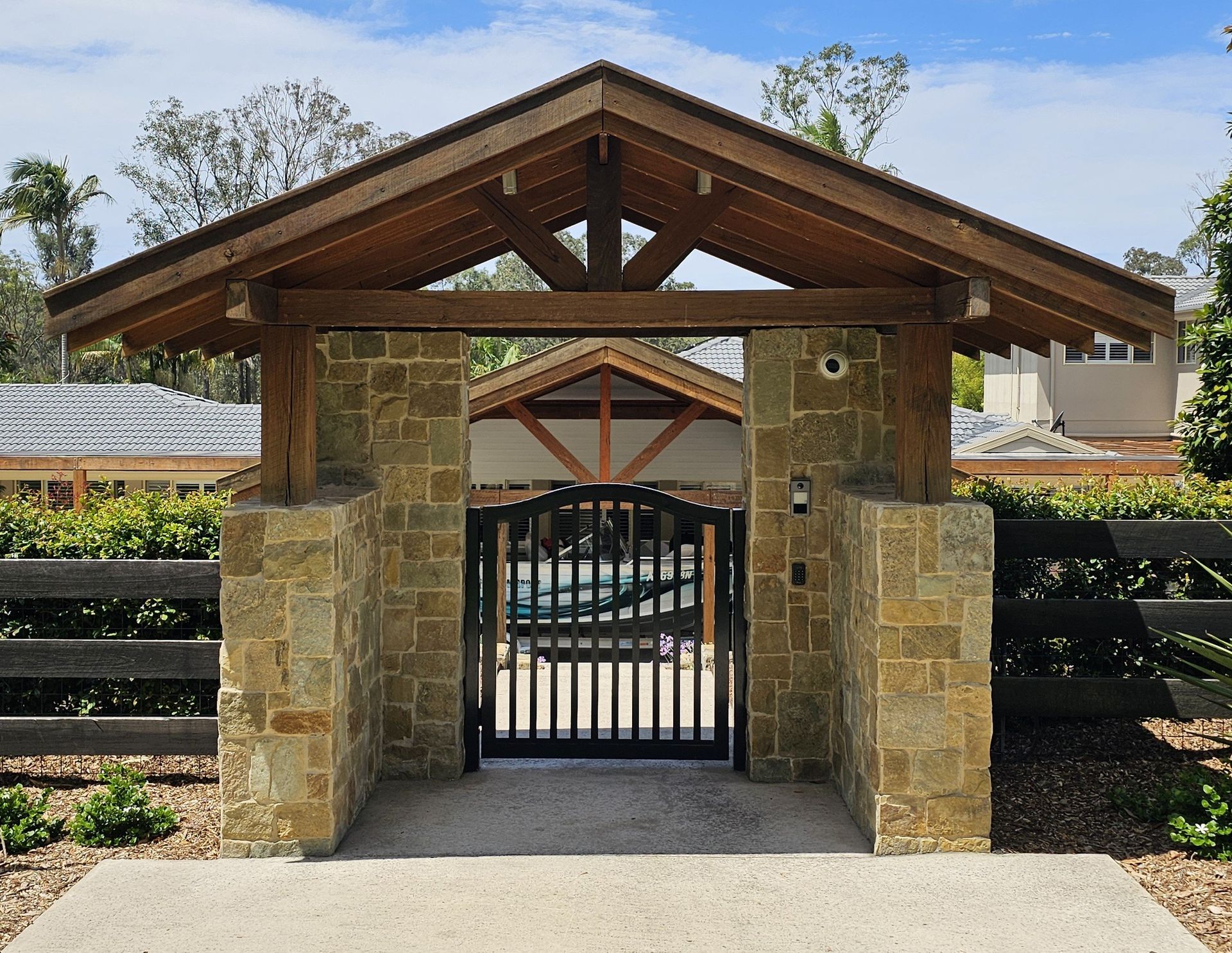 Stone and wood gate entrance with slatted black gate, beneath a peaked roof.