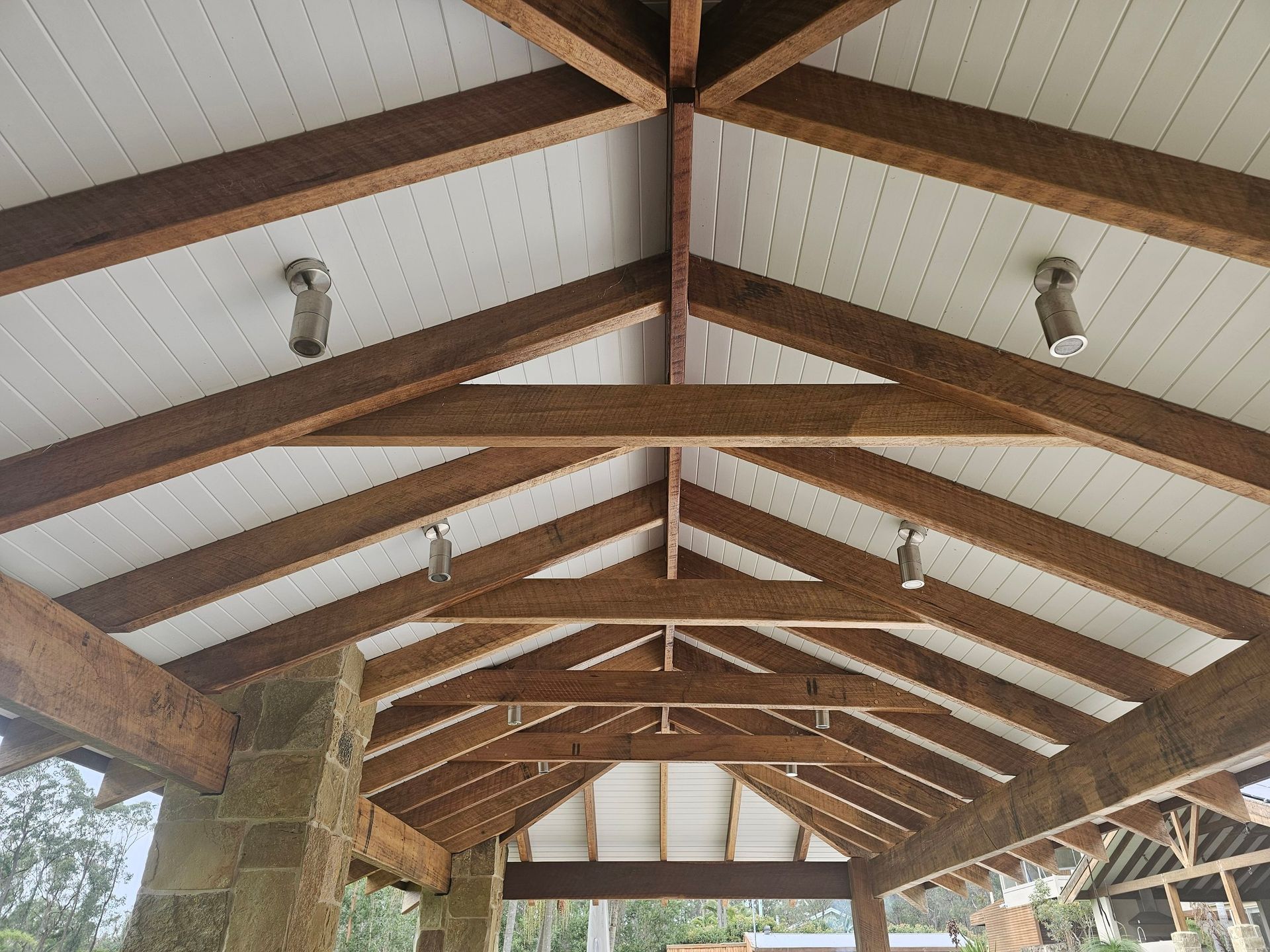 Wooden beamed ceiling with white panels, spotlights, and stone pillars.
