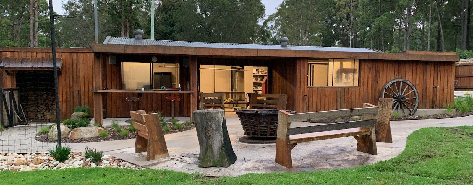 Tan building with garage, windows, and unfinished dirt/gravel yard in a wooded area.