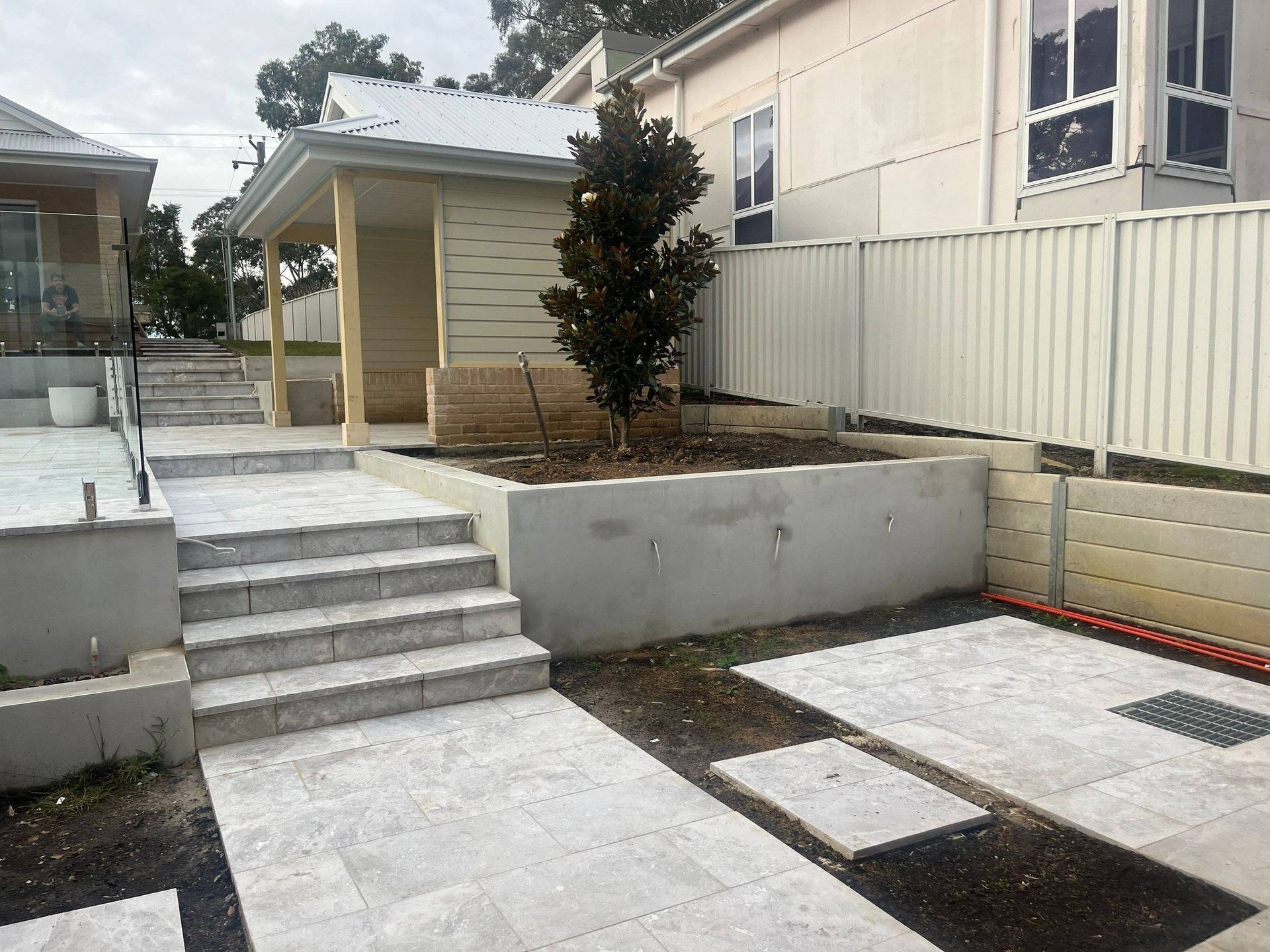 Stone steps lead up to a small building next to a paved area, bordered by a white fence.