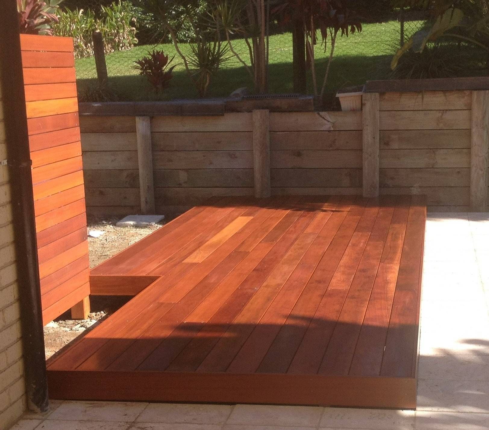 Wooden deck with rich brown planks on a concrete patio, adjacent to a wooden privacy screen.