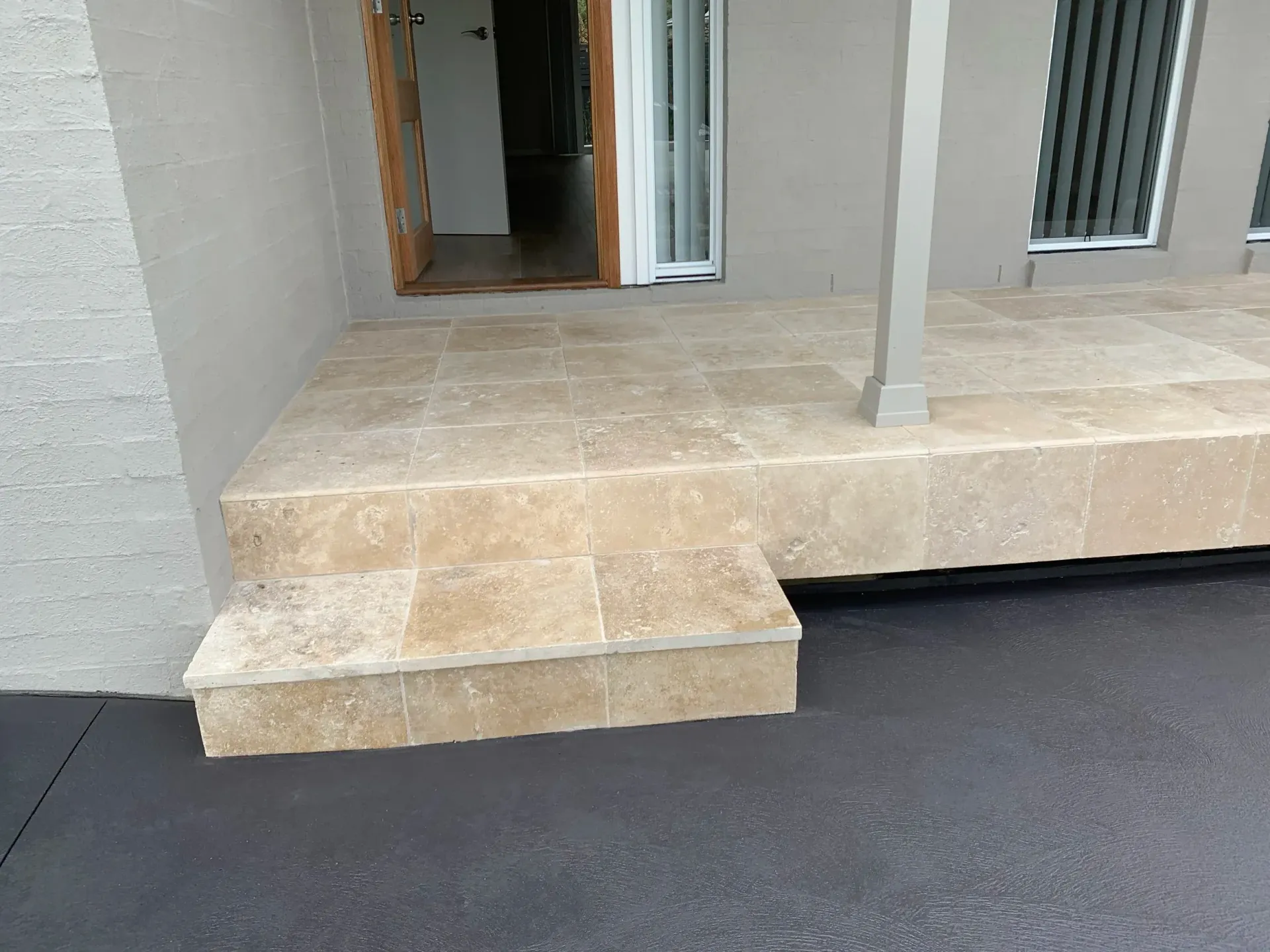 Stone steps lead up to a doorway and porch. Grey painted walls, dark pavement.