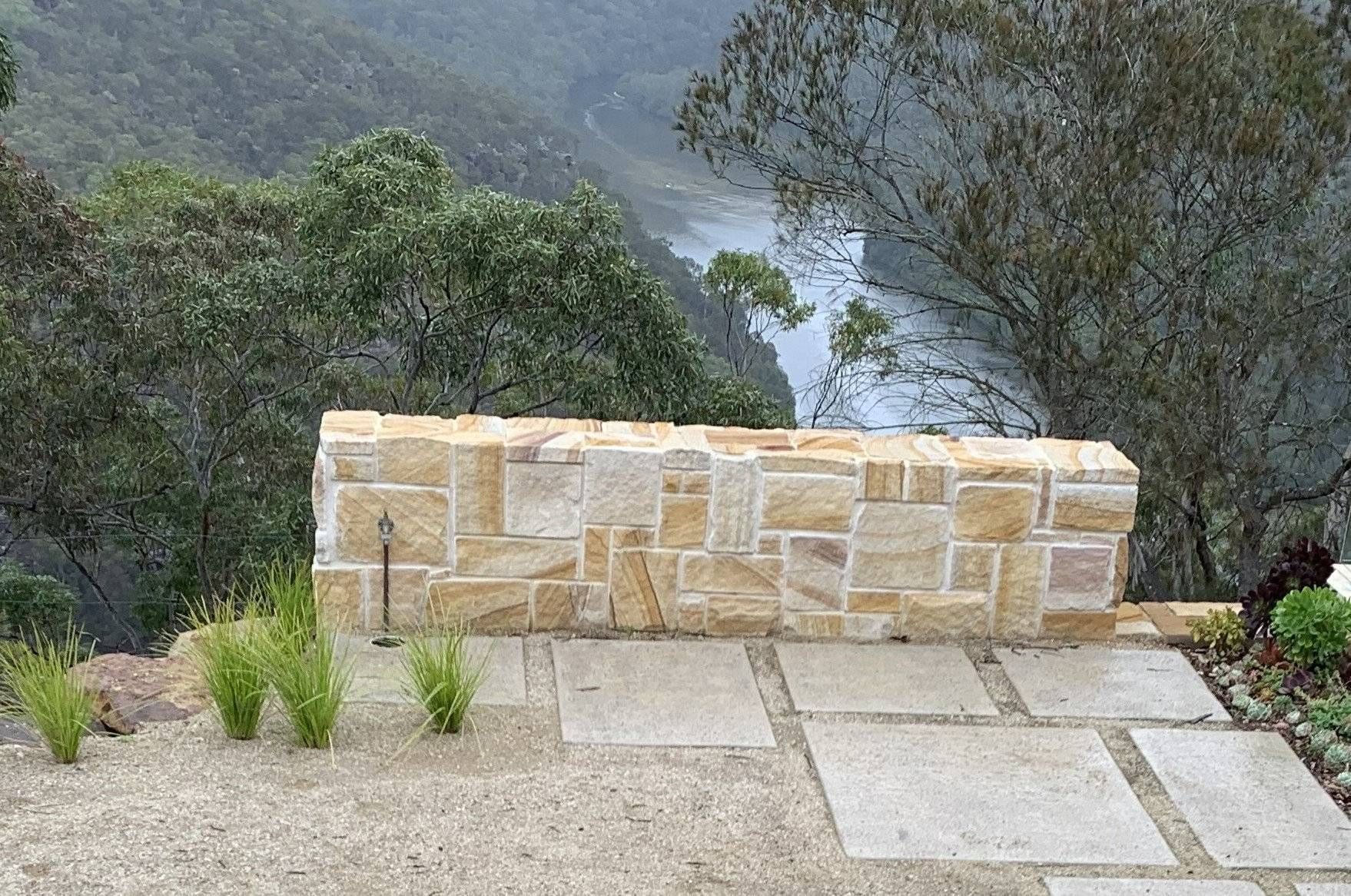 Stone wall overlooking a river valley; tan stone with gray concrete tiles.