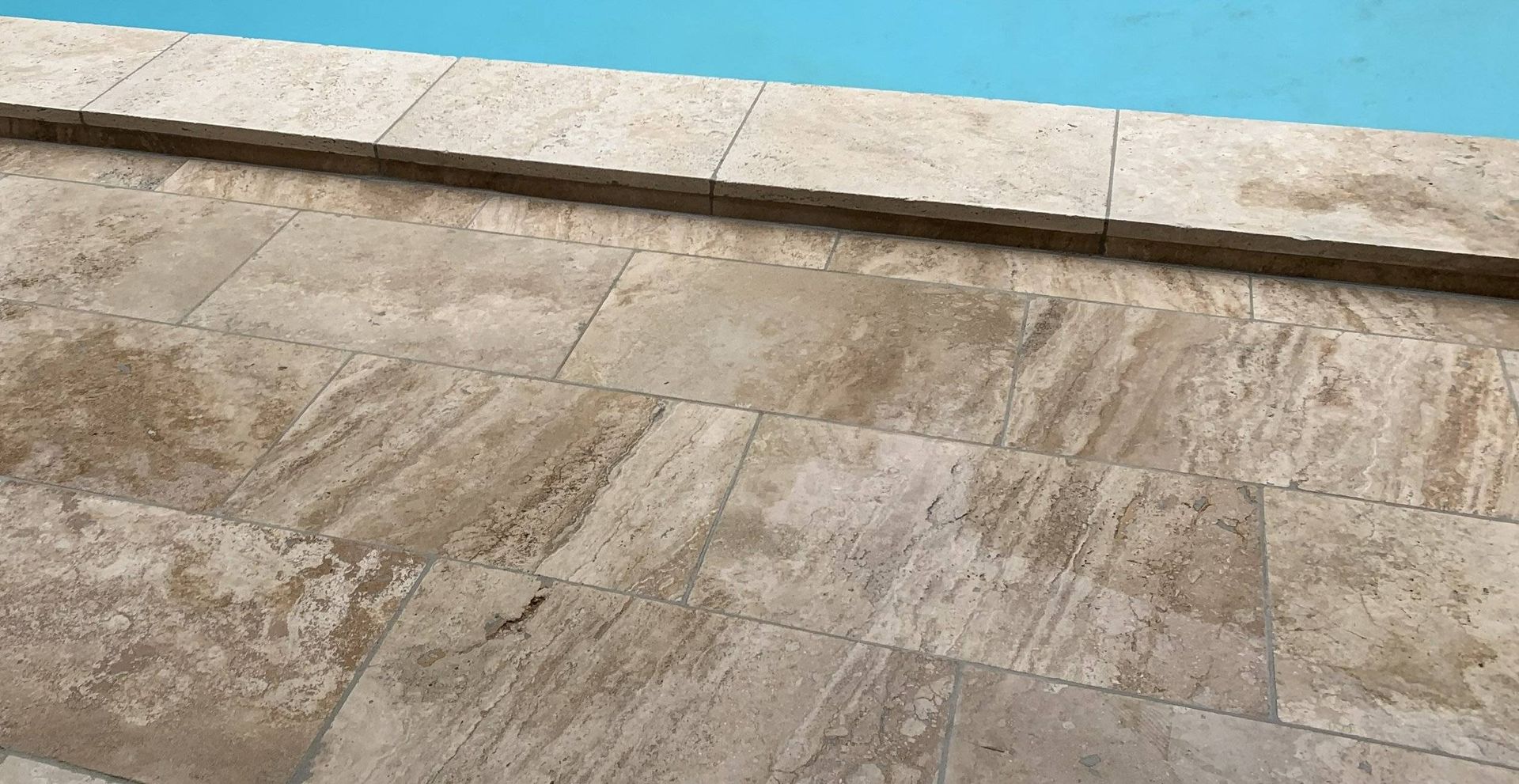 Beige stone tiles next to blue pool water.