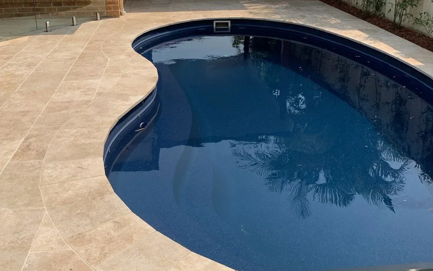 A kidney-shaped swimming pool with blue tile interior surrounded by tan tile patio.