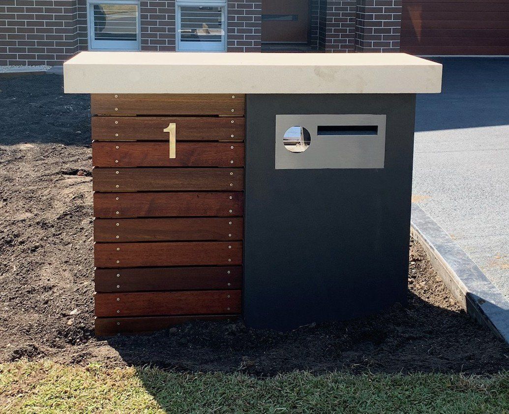 Modern mailbox with wood paneling and a dark gray body. A concrete cap and the number 