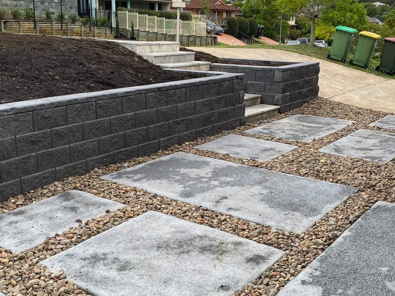 Retaining wall and stone pavers with gravel in a landscaped front yard.