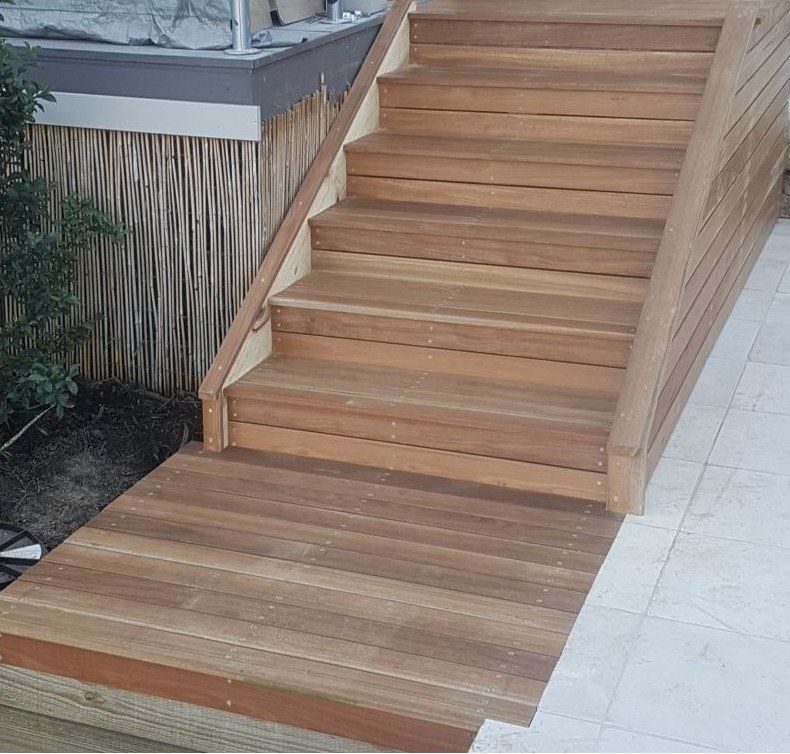 Wooden outdoor stairs and ramp leading upwards, next to a bamboo-like screen.
