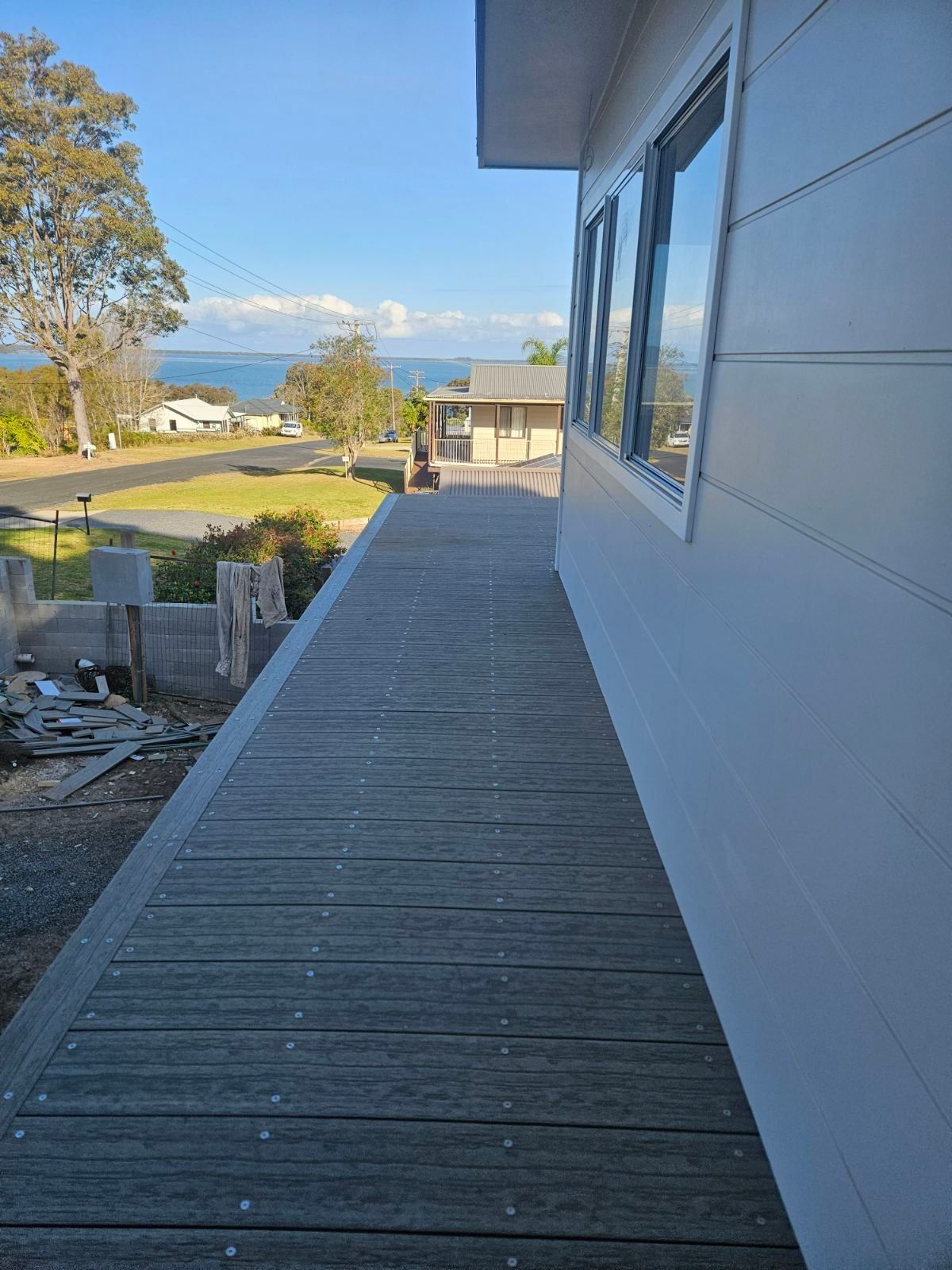 Wooden deck alongside a white house with windows, overlooking a view of the sea and sky.