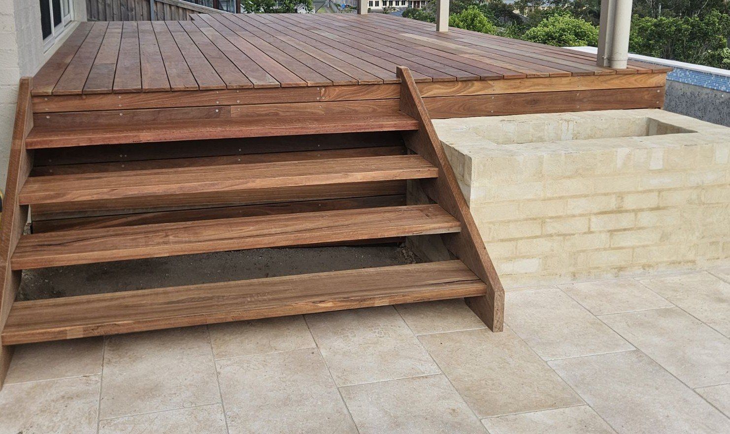 Wooden deck with steps and a brick feature, outdoors.