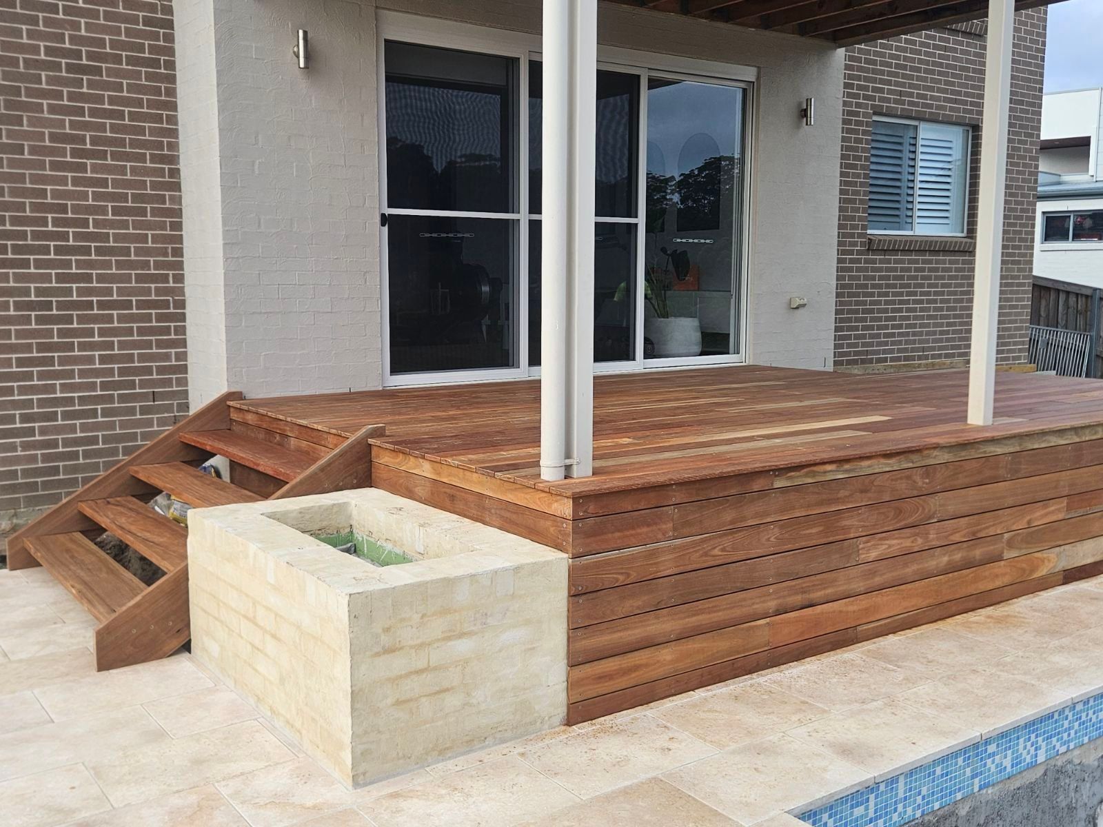 Wooden deck and steps next to a brick building. Planter box is in front. Pool visible below.