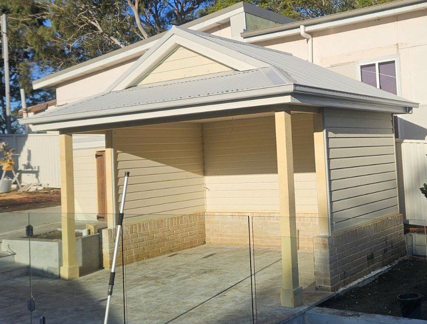 Carport with gray roof, beige siding, and wooden posts under construction.