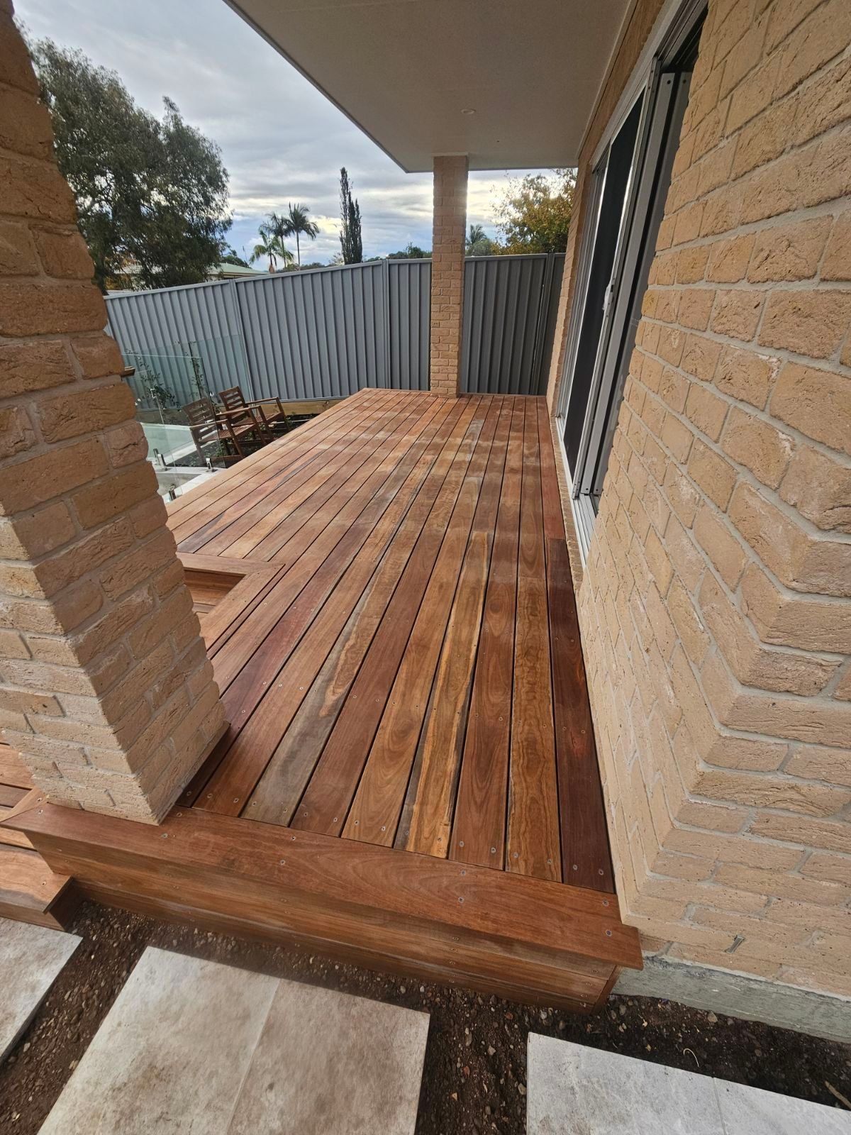 Wooden deck with brick columns and side of a house, exterior shot.