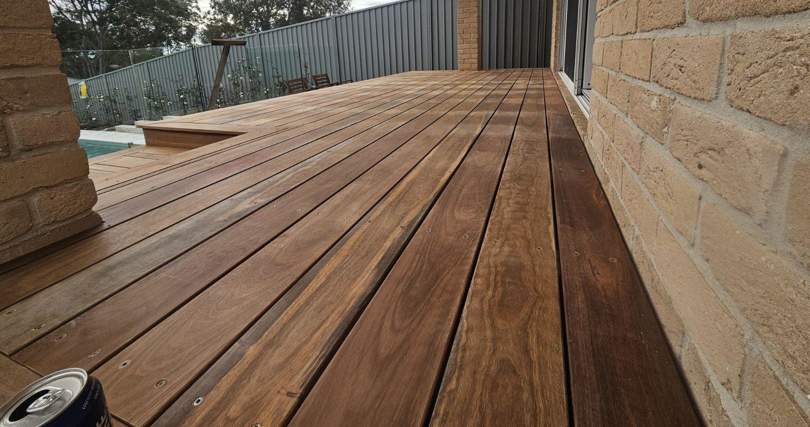 Wooden deck extending from a brick wall, with a metal fence in the background.