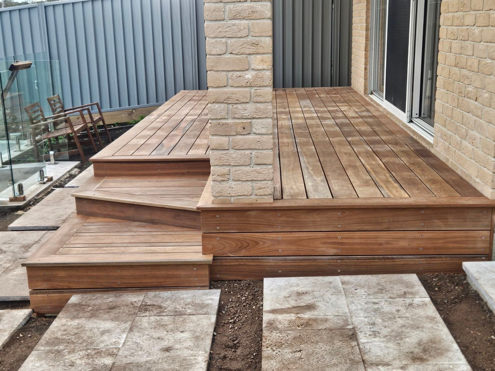Wooden deck with steps and stone pavers, next to a brick wall.