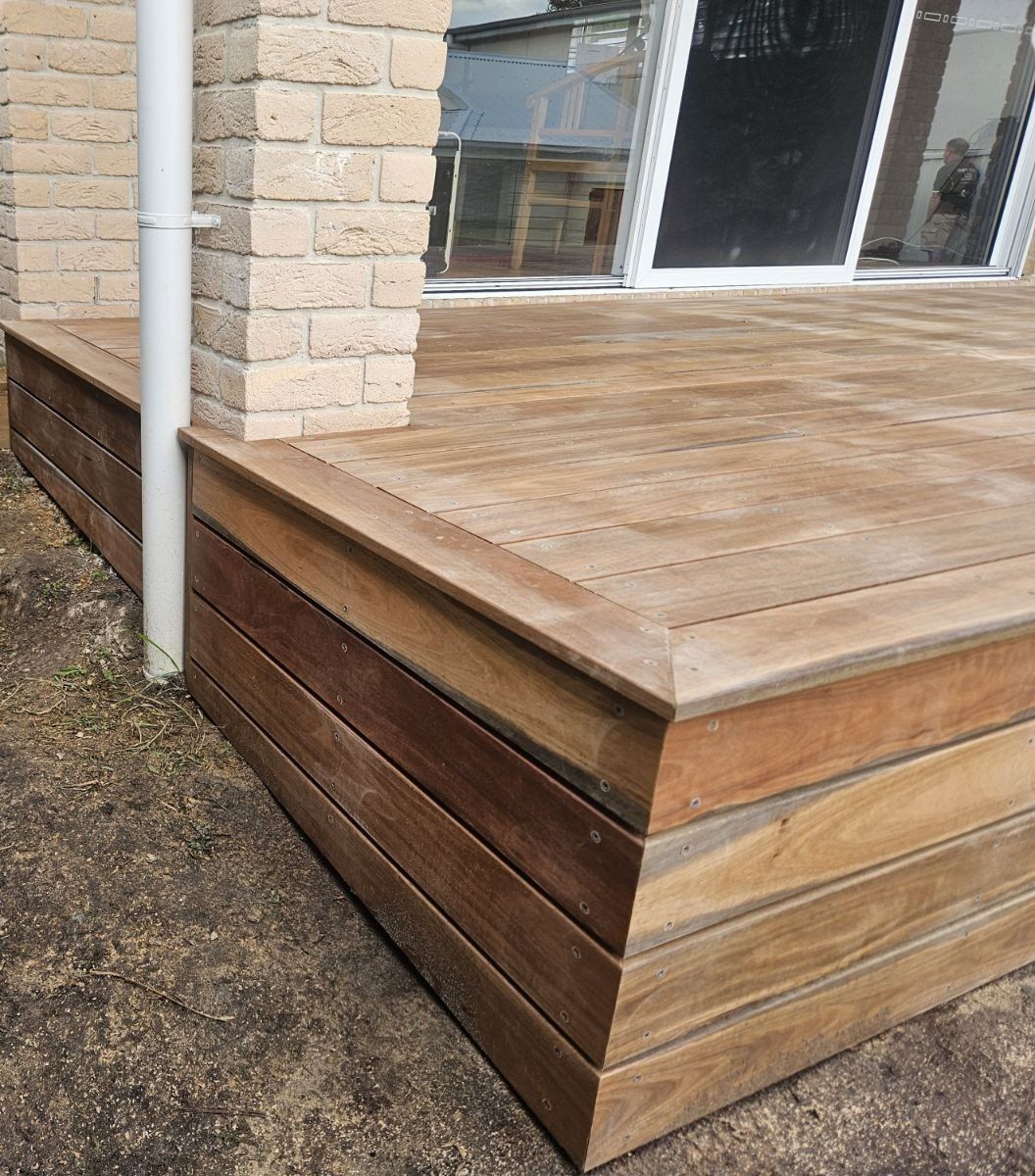 Wooden deck with a brick pillar, next to a window; outdoor setting.