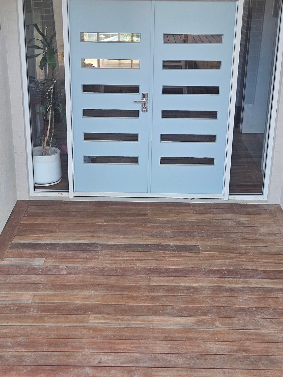 Blue double doors with horizontal window panes, flanked by sidelights. Brown wooden deck.