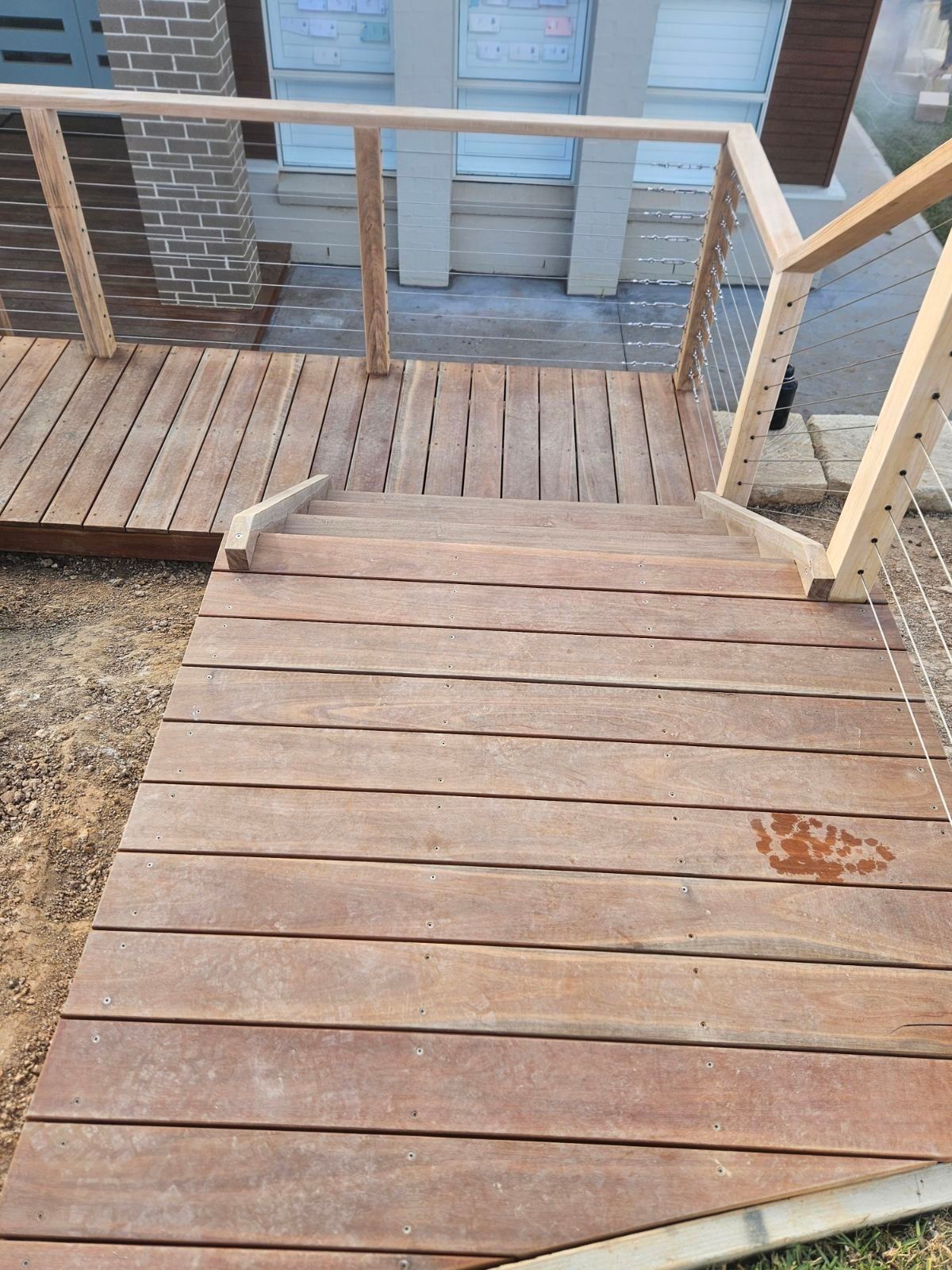 Wooden stairs and ramp leading to a house, with metal cable railings.