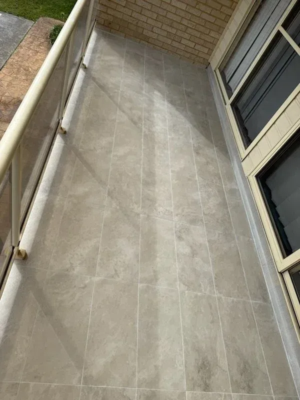 Balcony with light grey tiled floor, brick wall, and beige window frame.