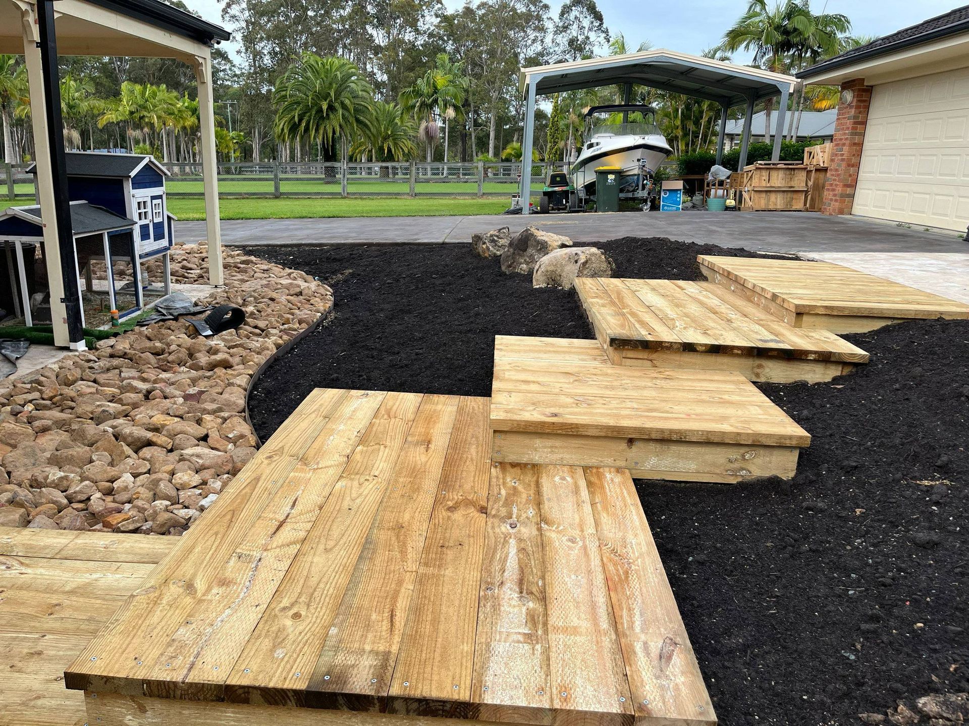 Wooden stepping stones through black mulch in a yard.