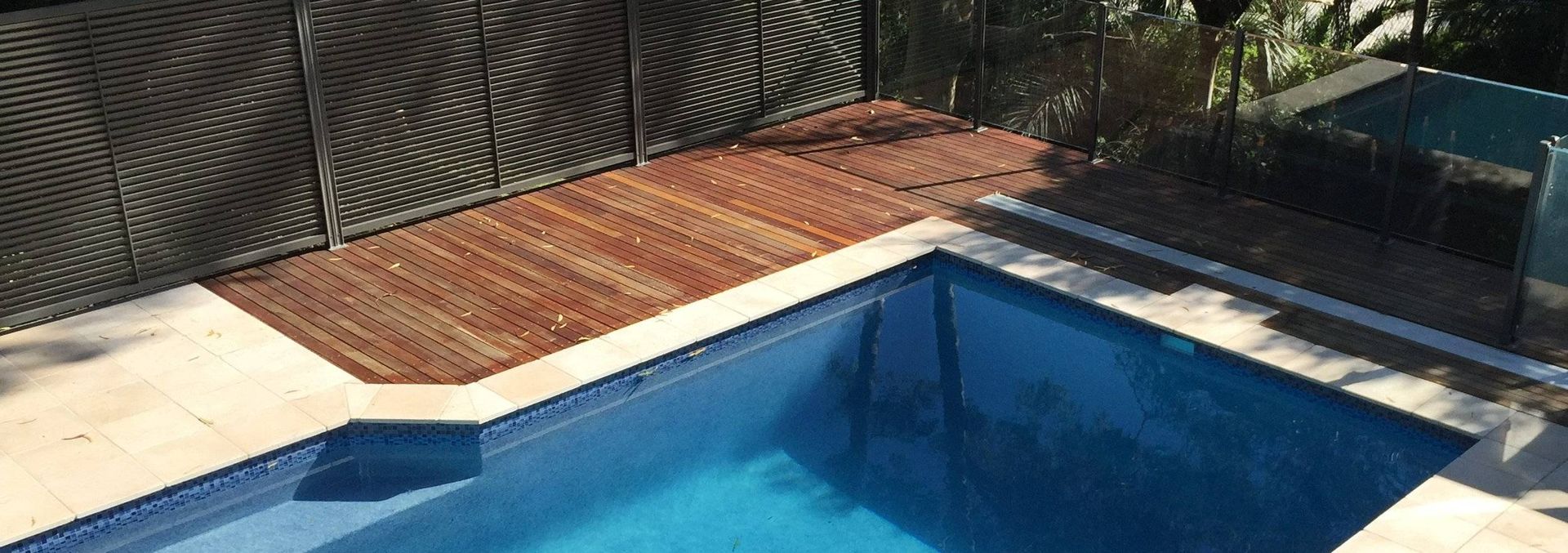 A swimming pool with blue water and wooden decking surrounded by a brown fence.