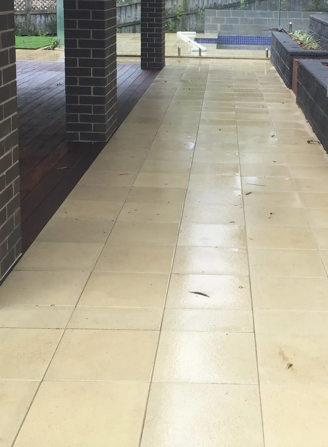 Exterior patio with beige stone tiles and brick columns, wet from rain.