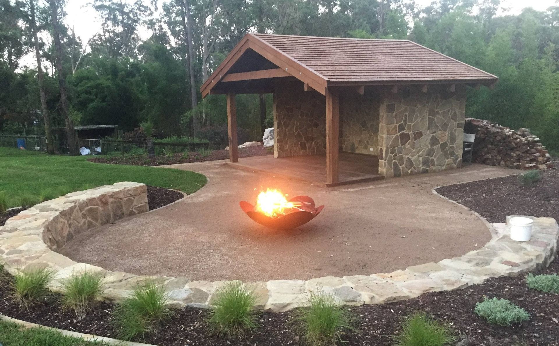 Fire pit area with stone walls, a shelter, and burning flames outdoors.