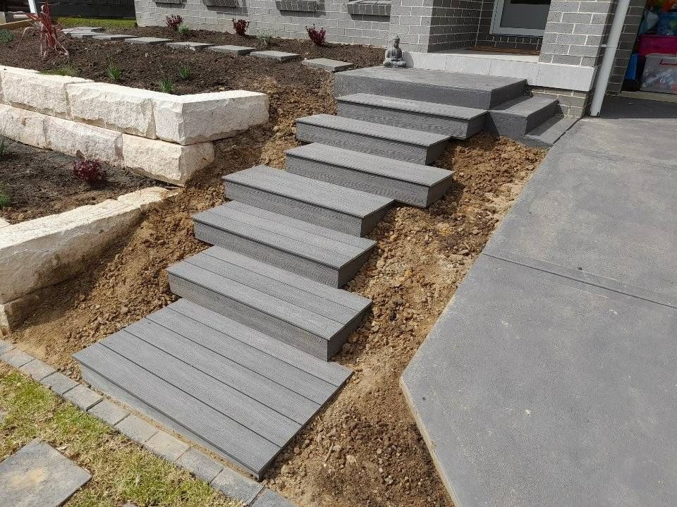 Gray composite steps leading up a slope next to a concrete driveway and retaining wall.