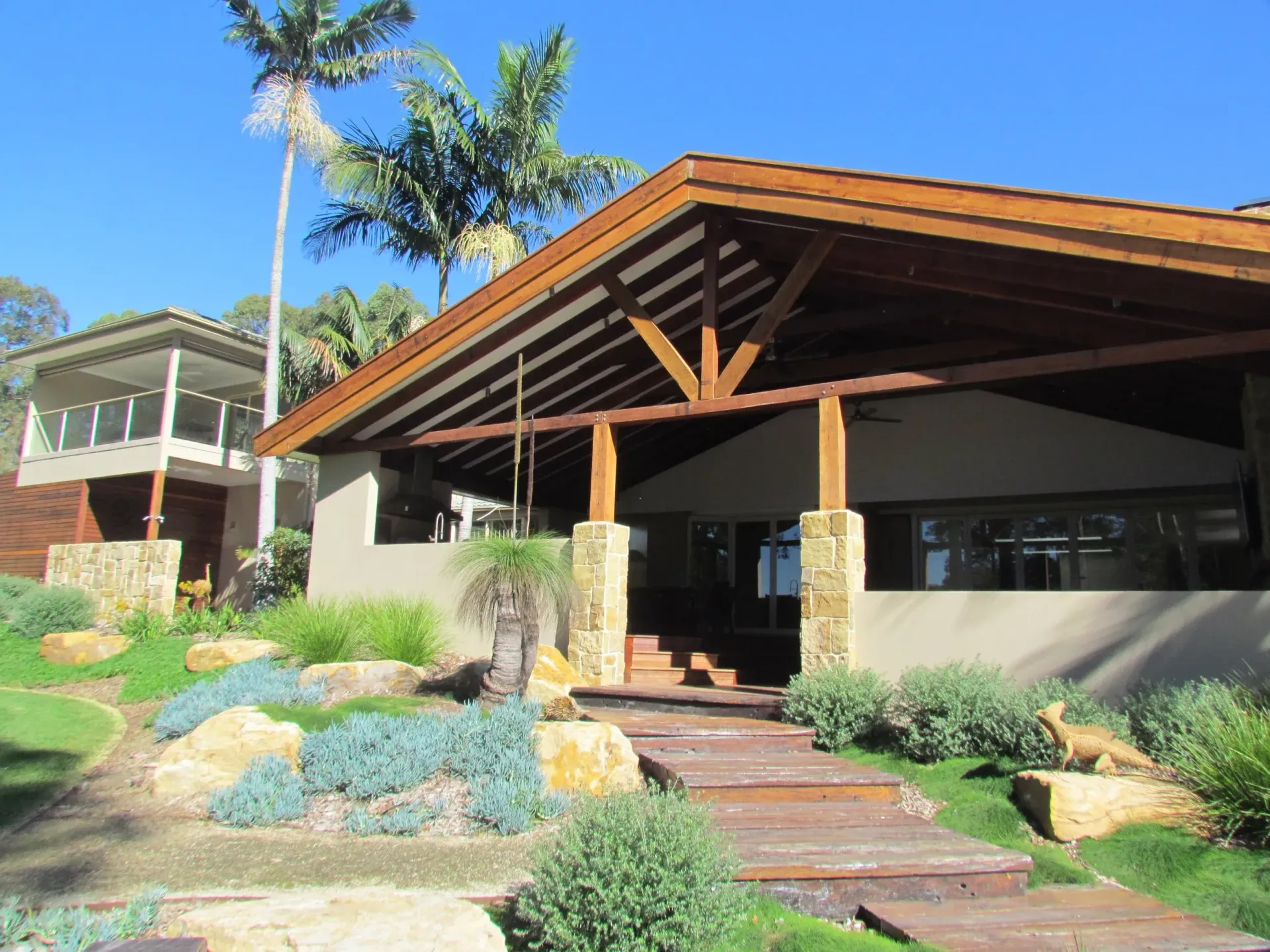 A modern, open-air home with wooden roof and supports, stone pillars, and landscaped yard.