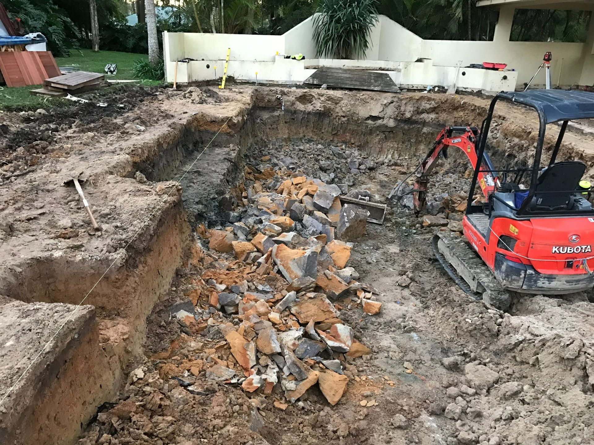 Construction site with a mini excavator digging a pool, dirt, and rocks.