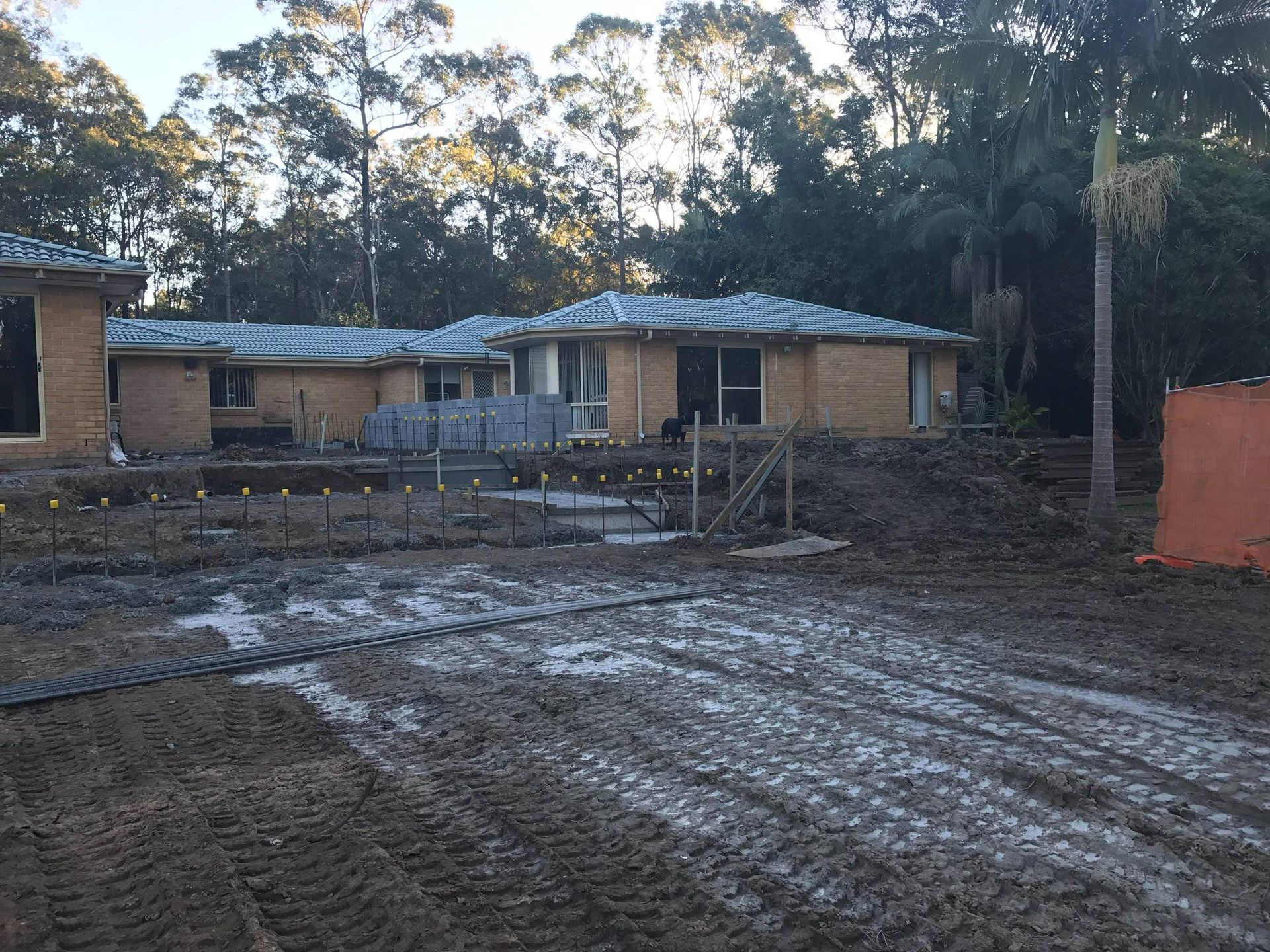 Construction site: partially built brick houses with dirt, wood supports, and muddy ground.
