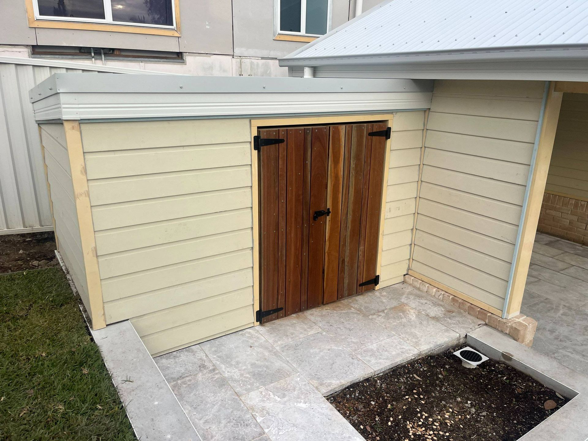 Wooden storage shed with brown door, light beige siding, and gray trim.
